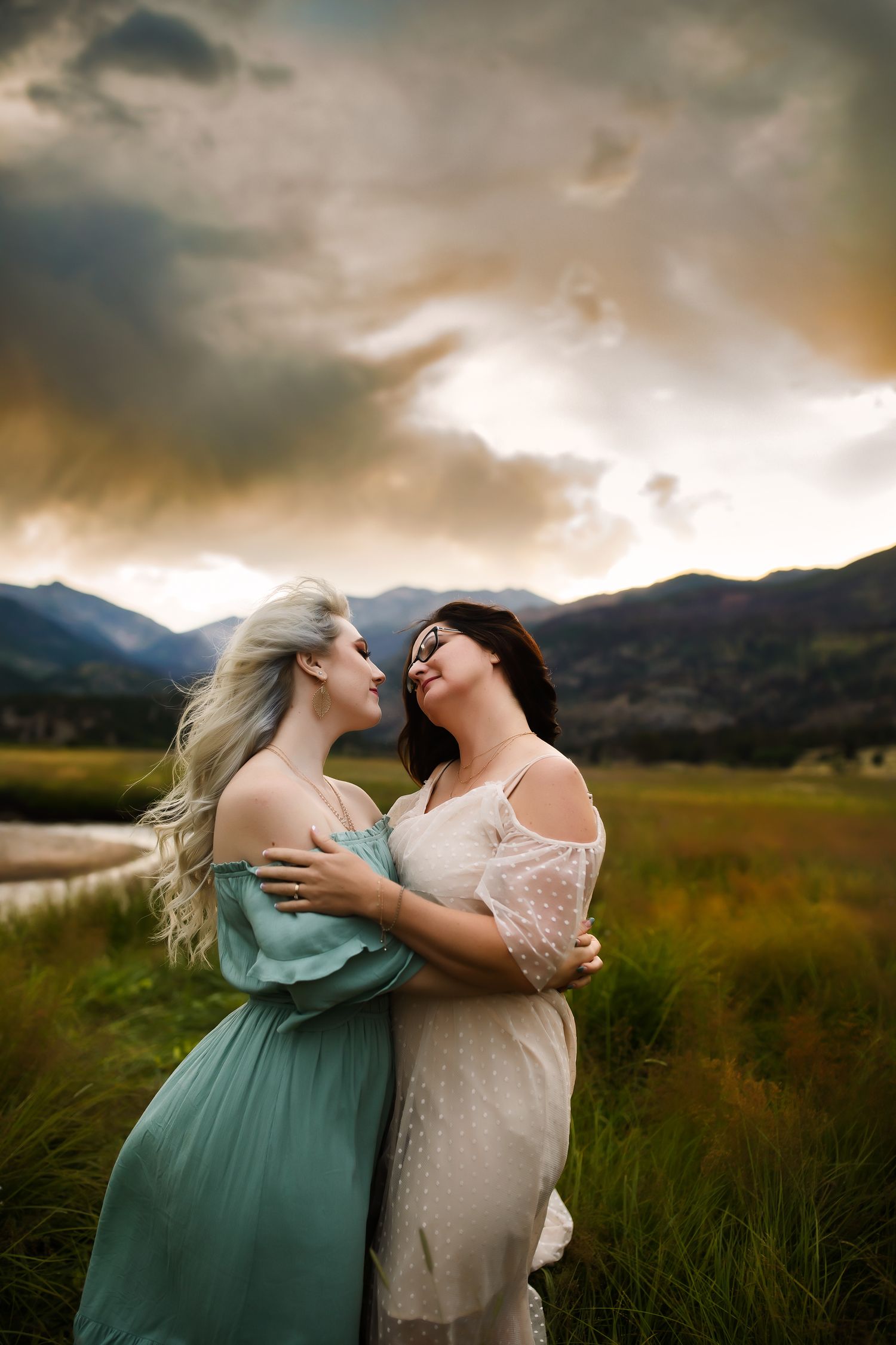Two people sharing an intimate moment in a mountain field at sunset.