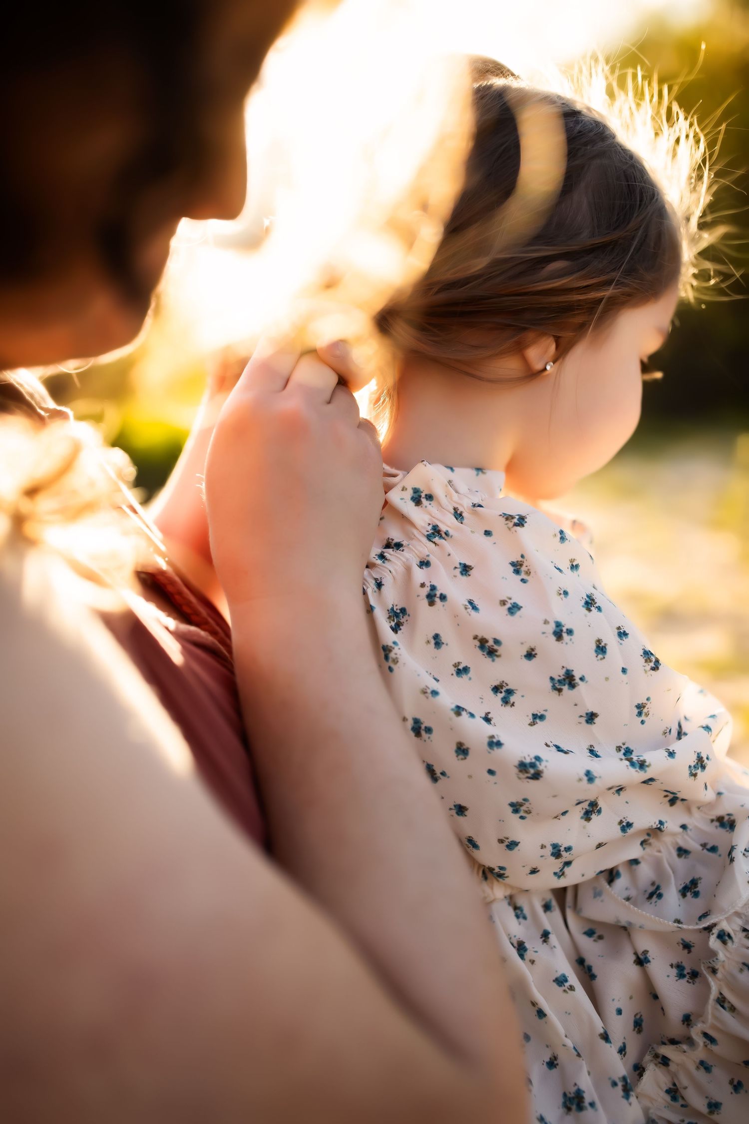 Close-up shot of a couple embracing during golden hour with a floral patterned dress visible.
