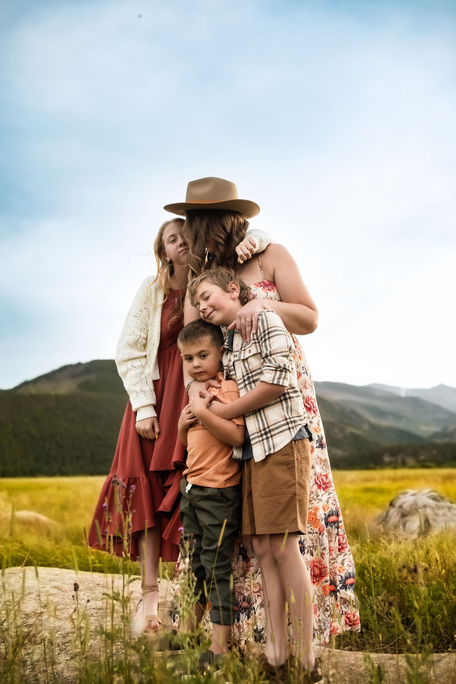 A tender family moment captured in a golden field with mountains in the background.