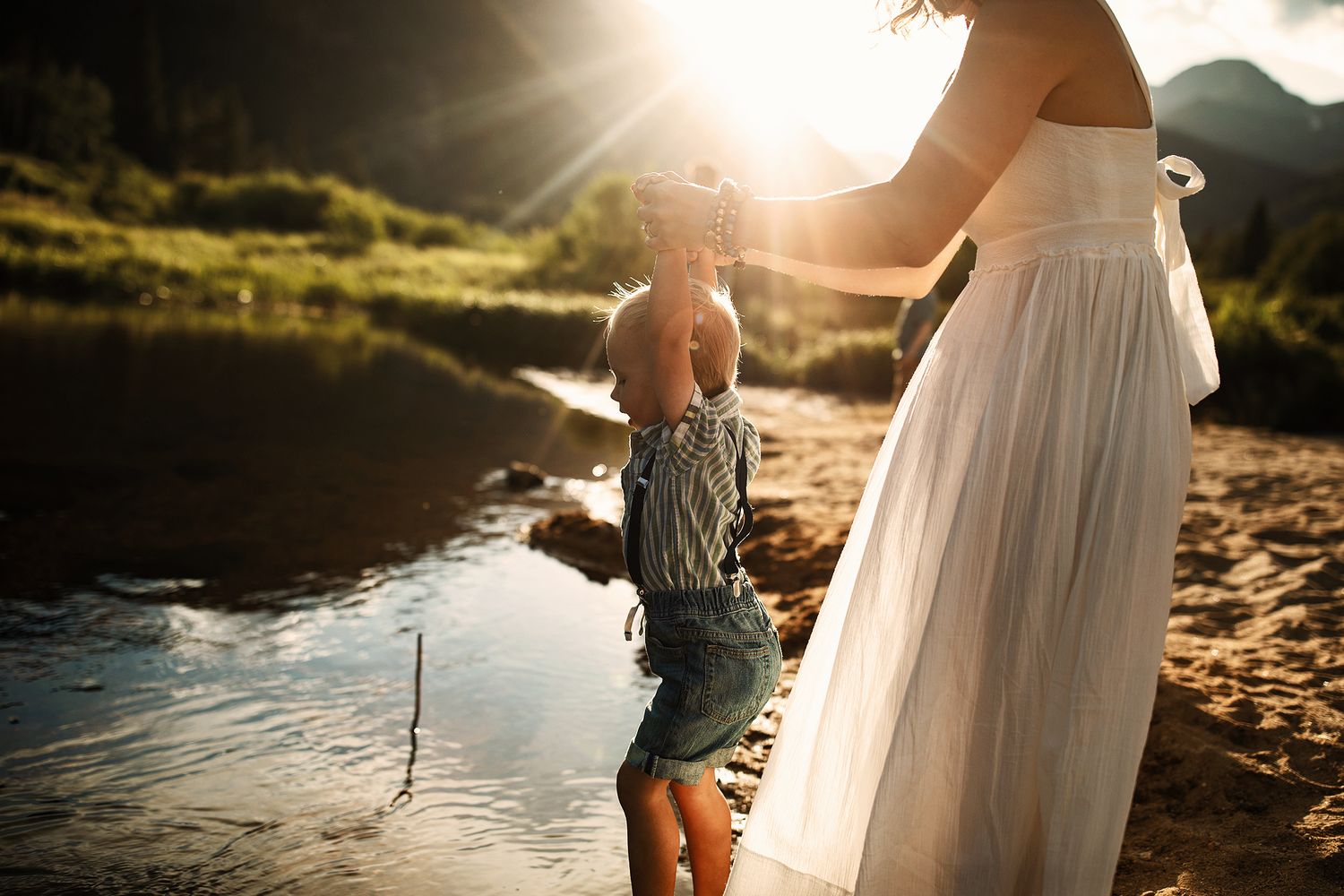 Couple walking along a sunlit riverbank during golden hour creating romantic silhouettes.