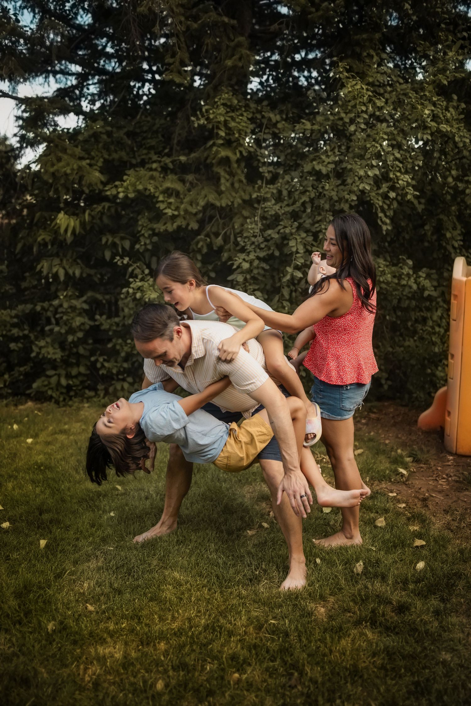 Playful sequence of people falling backwards onto grass in a backyard setting.