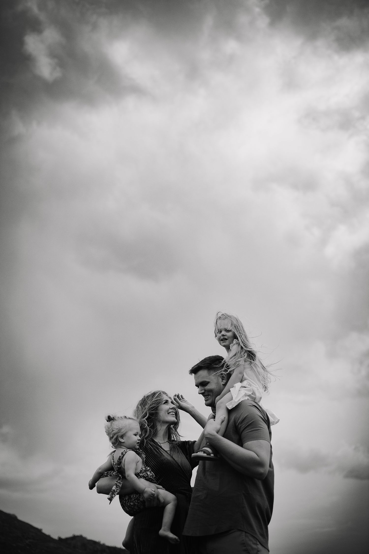 Dramatic black and white portrait of a couple sharing intimate moments against cloudy sky.