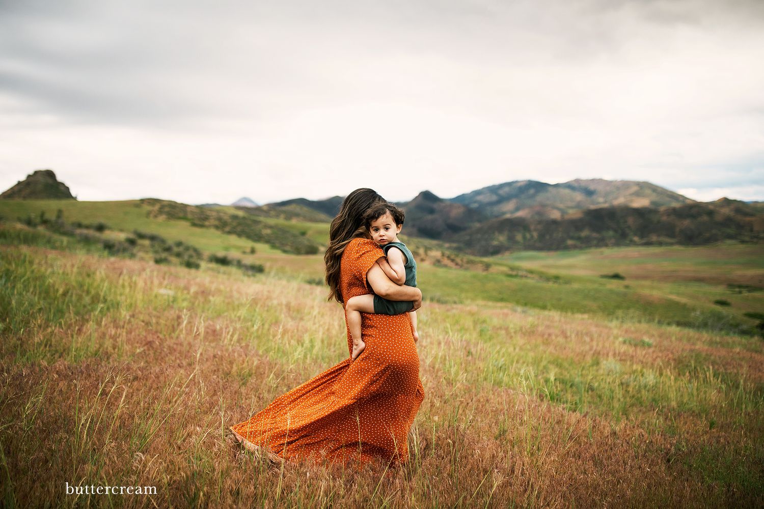 Orange dress billowing in wind against dramatic mountain landscape.