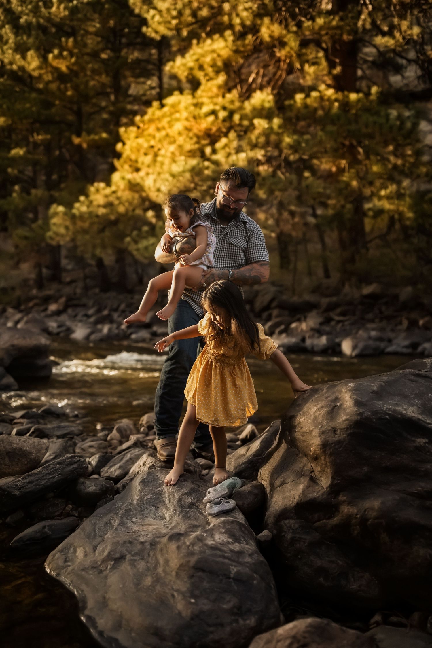 People carefully traversing rocky riverbed in golden forest light.