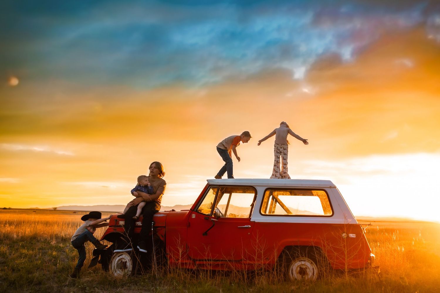 Silhouettes of people playing around a vintage truck during a dramatic sunset.