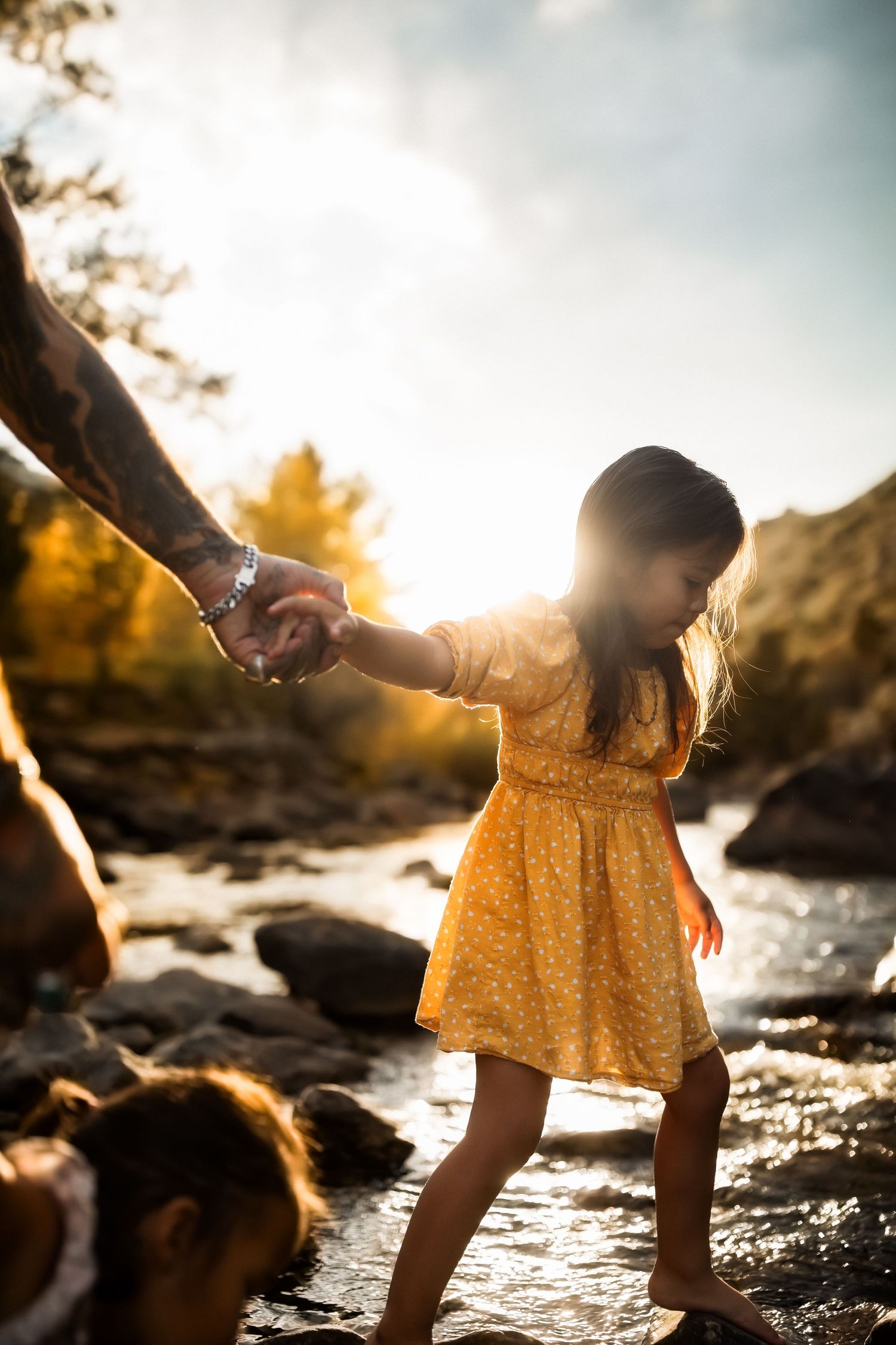 Child in yellow dress playing by water's edge during golden hour sunset.