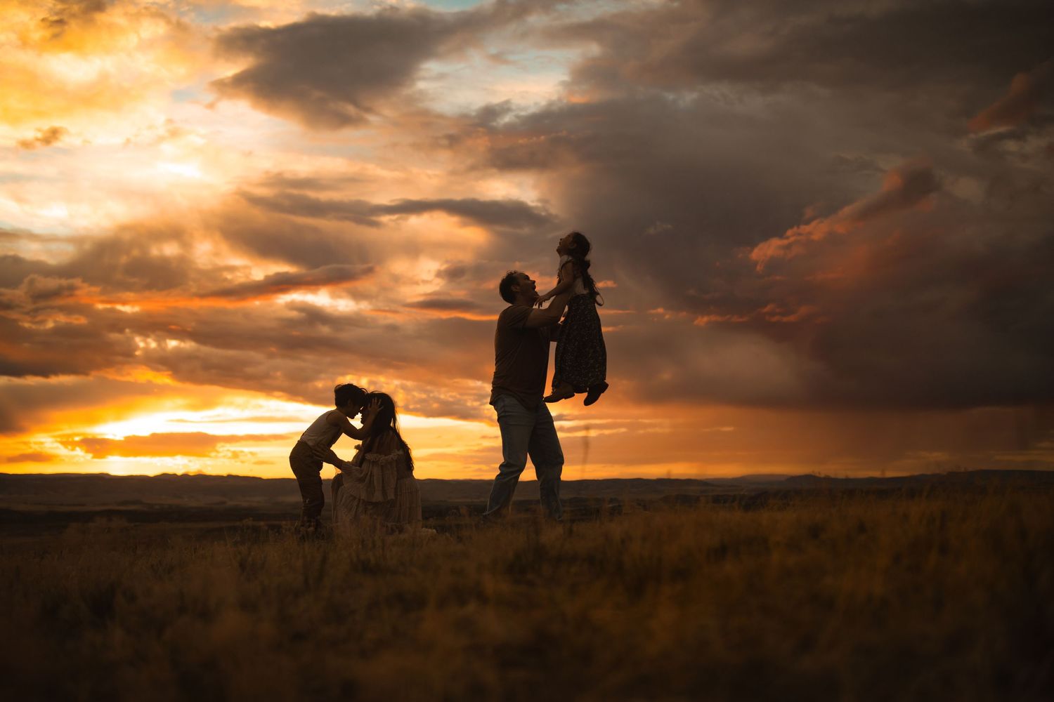Silhouettes of people embracing against a dramatic orange sunset sky.