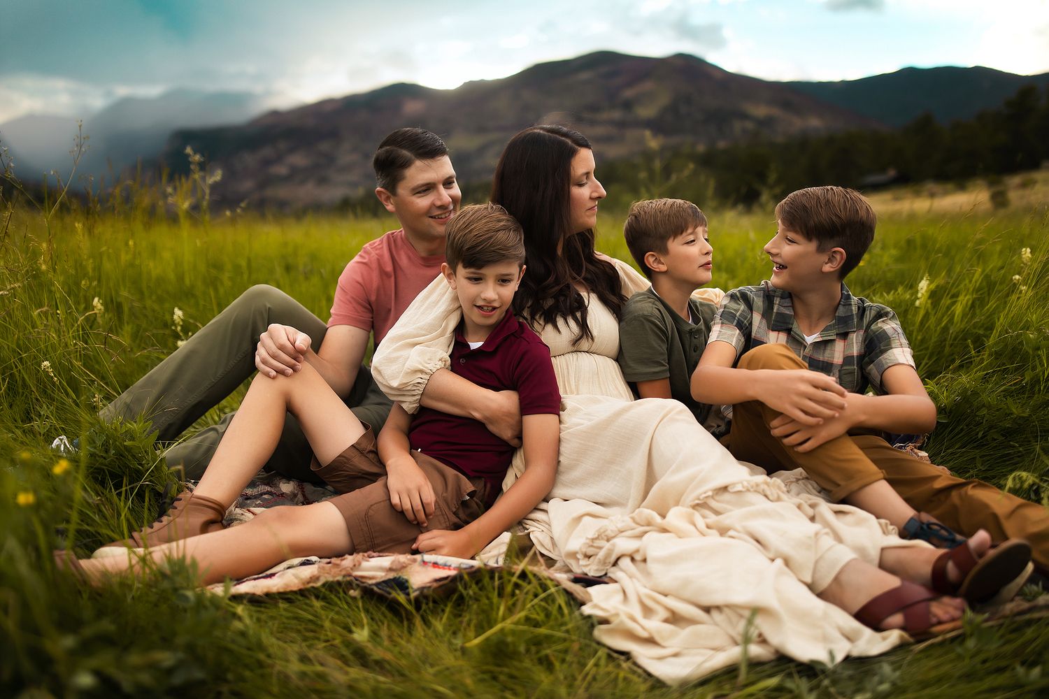 Family relaxing together in mountain meadow during golden hour.