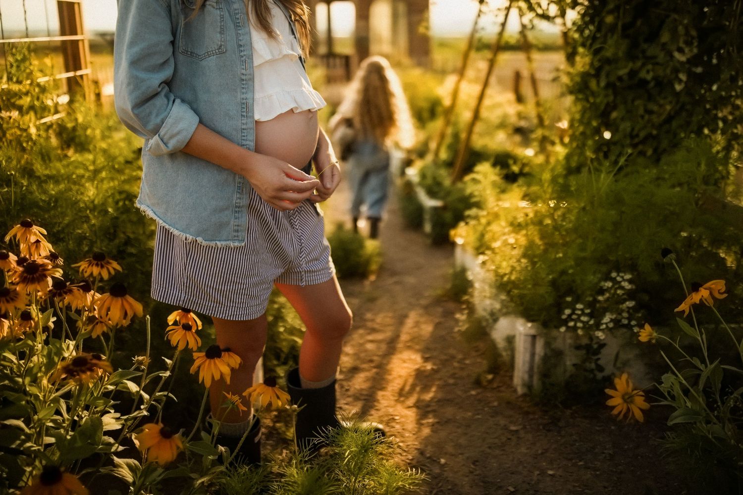 Couple embraces in a golden-lit garden path during sunset with flowers and trees creating a romantic atmosphere.