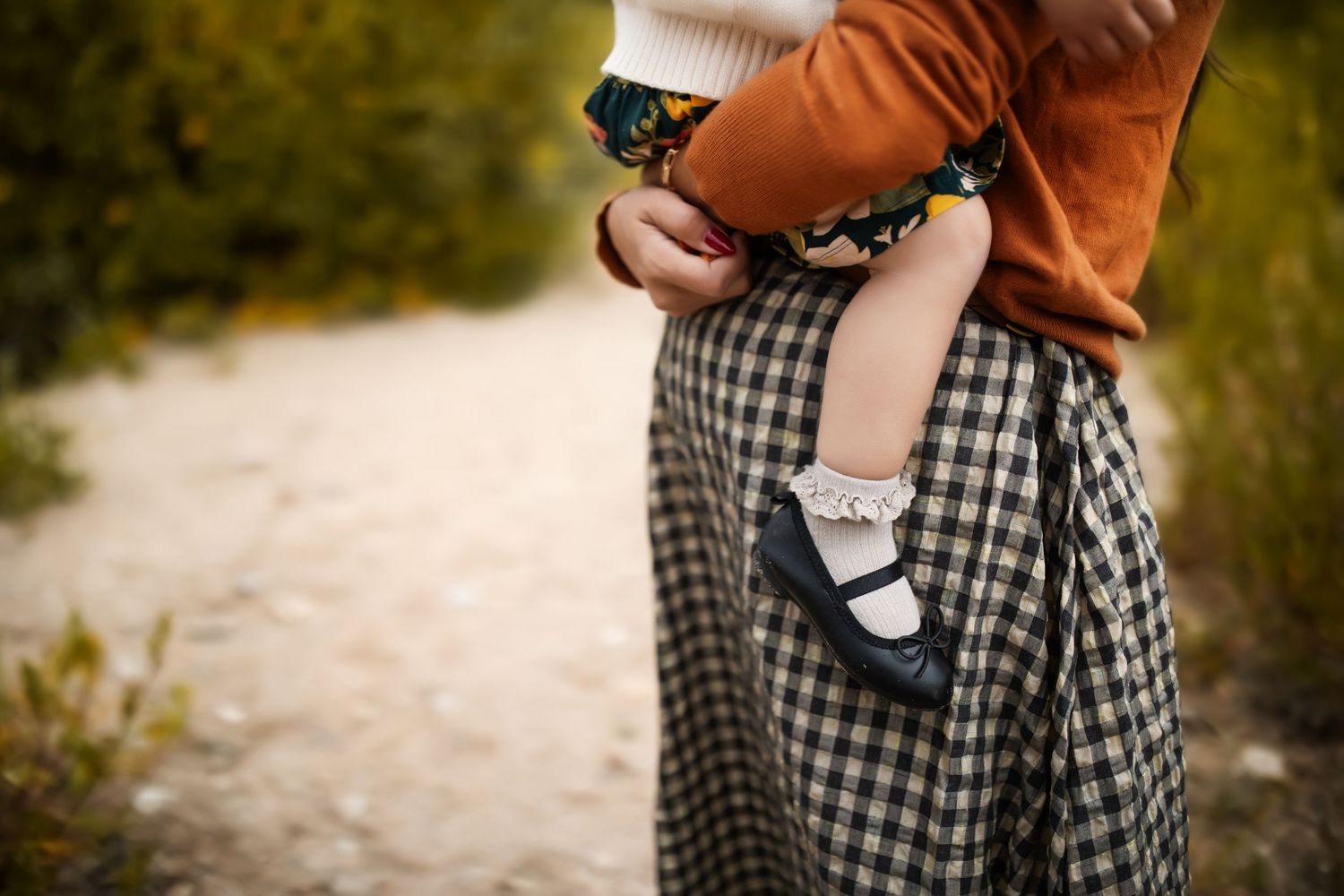 Close-up view of tiny feet in black and white shoes against checkered fabric outdoors.
