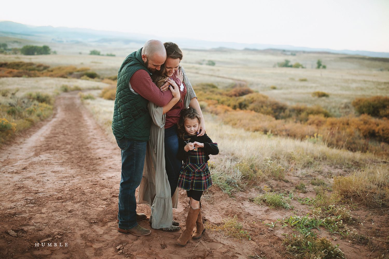 Family walking together on a winding dirt path through grassy hills.