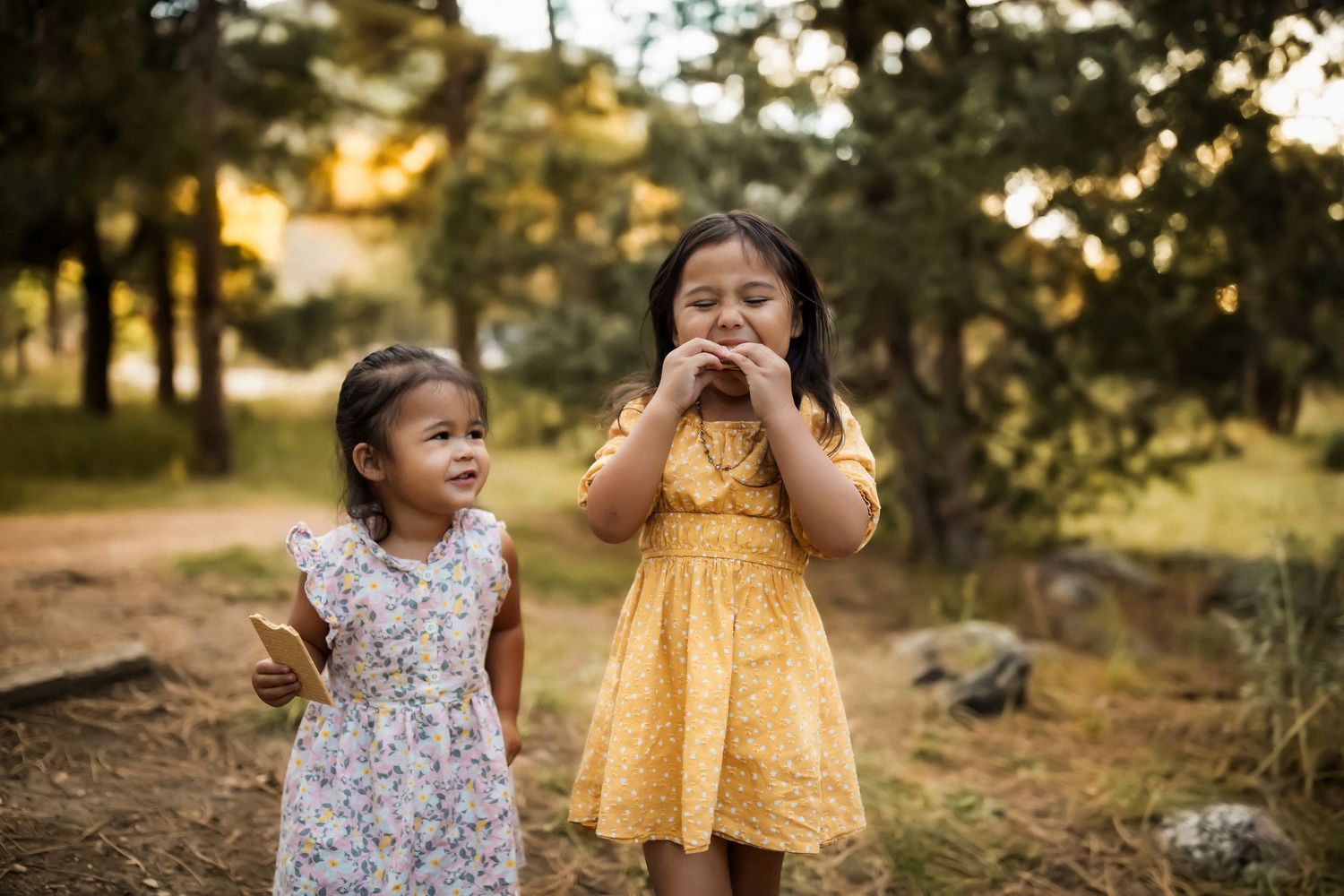 Two children in summer dresses sharing a fun moment outdoors.