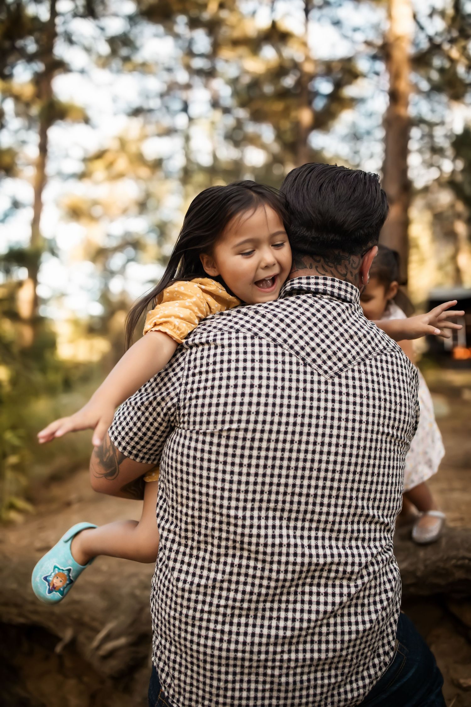 Playful embrace captured in a sunny forest setting with gingham shirt and yellow dress.