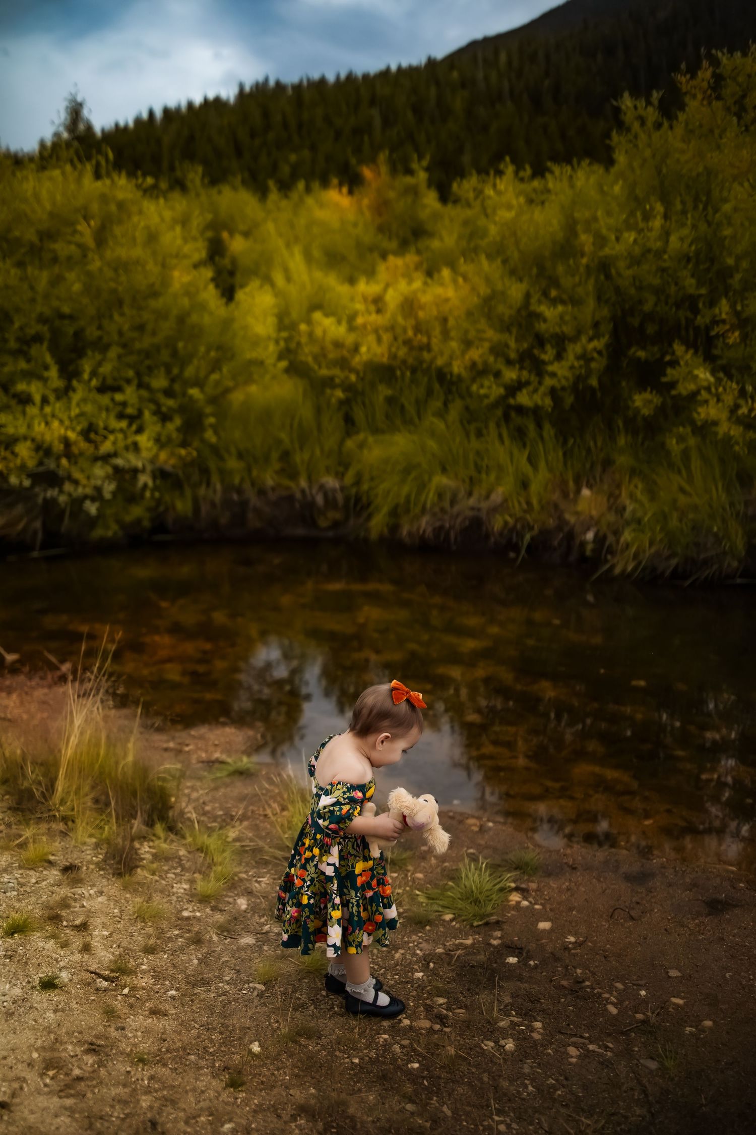 A couple shares an intimate moment on a riverbank surrounded by autumn foliage in a mountain landscape.