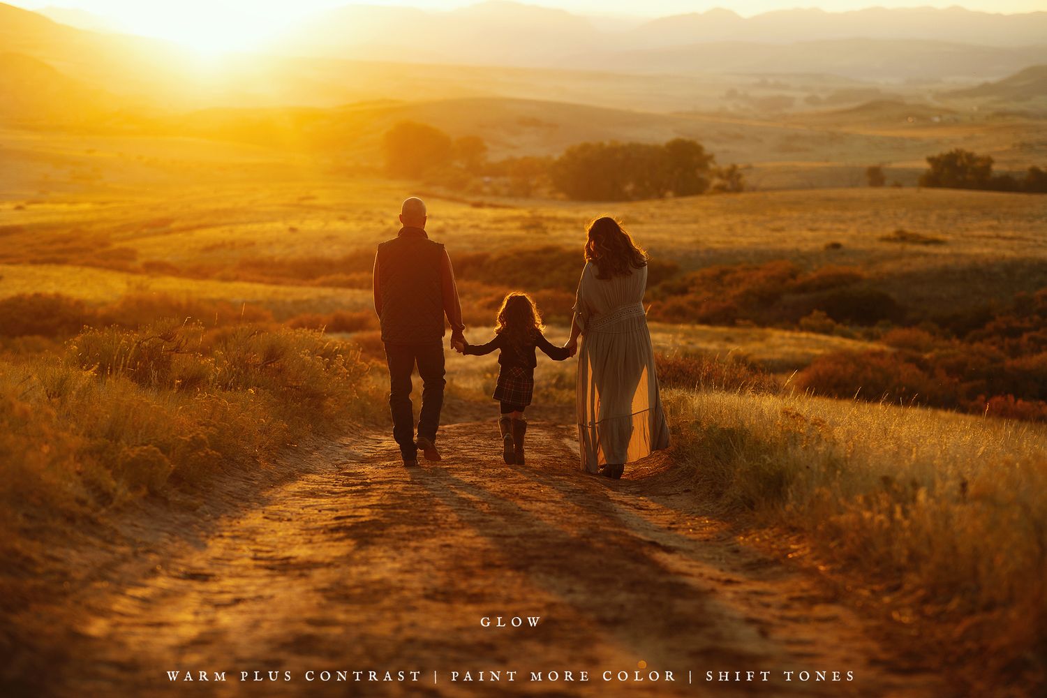 Silhouettes walking along a dirt path during golden hour in rolling hills.