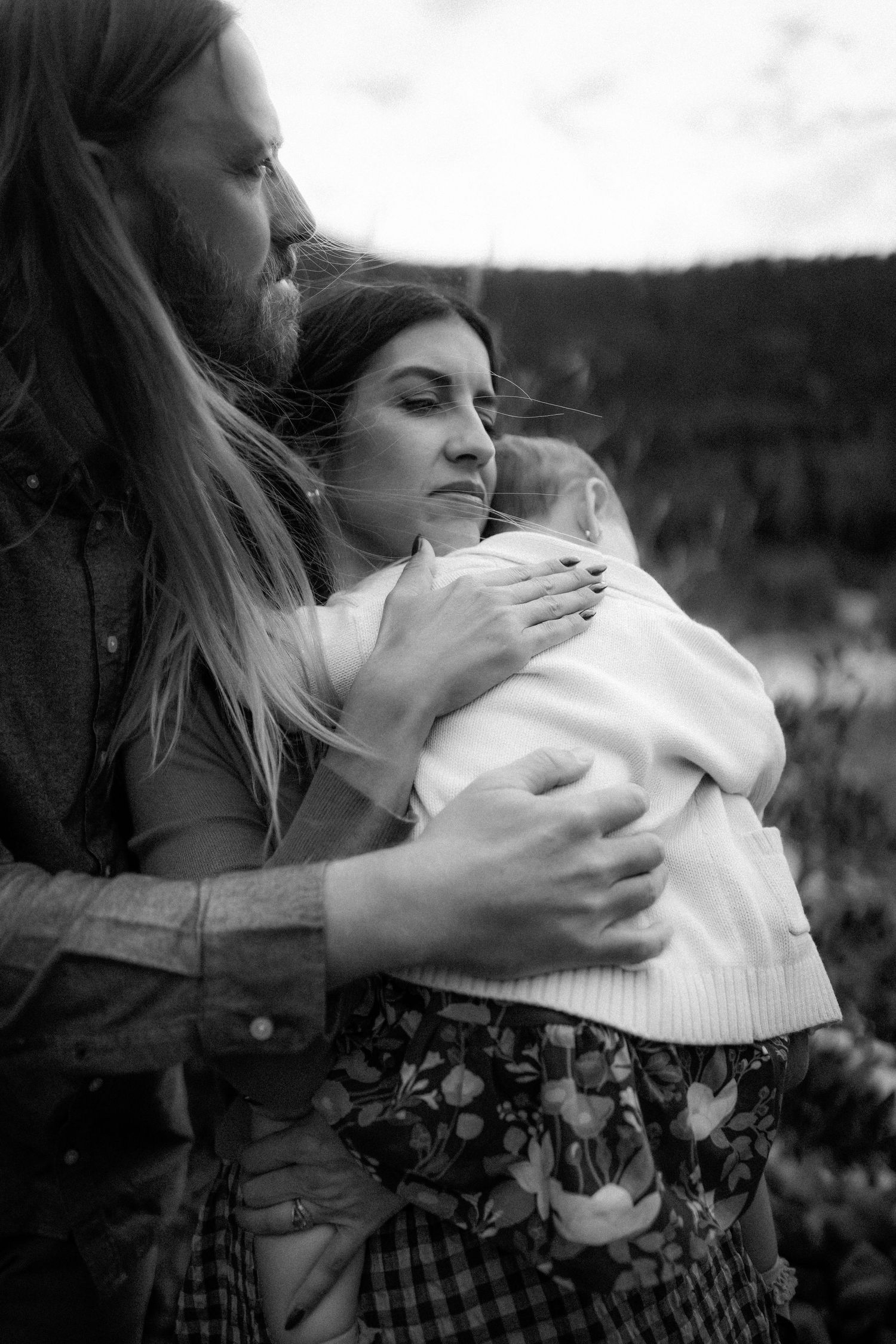 An intimate black and white portrait of a family embracing outdoors against a natural landscape.