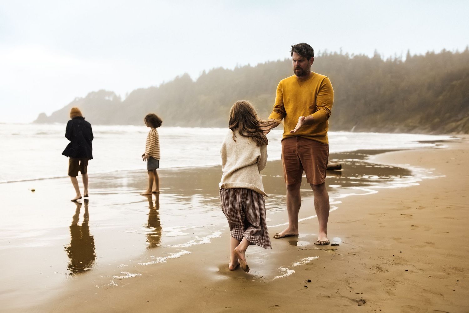 A family enjoys a peaceful morning walk along a misty Pacific Northwest beach at low tide.