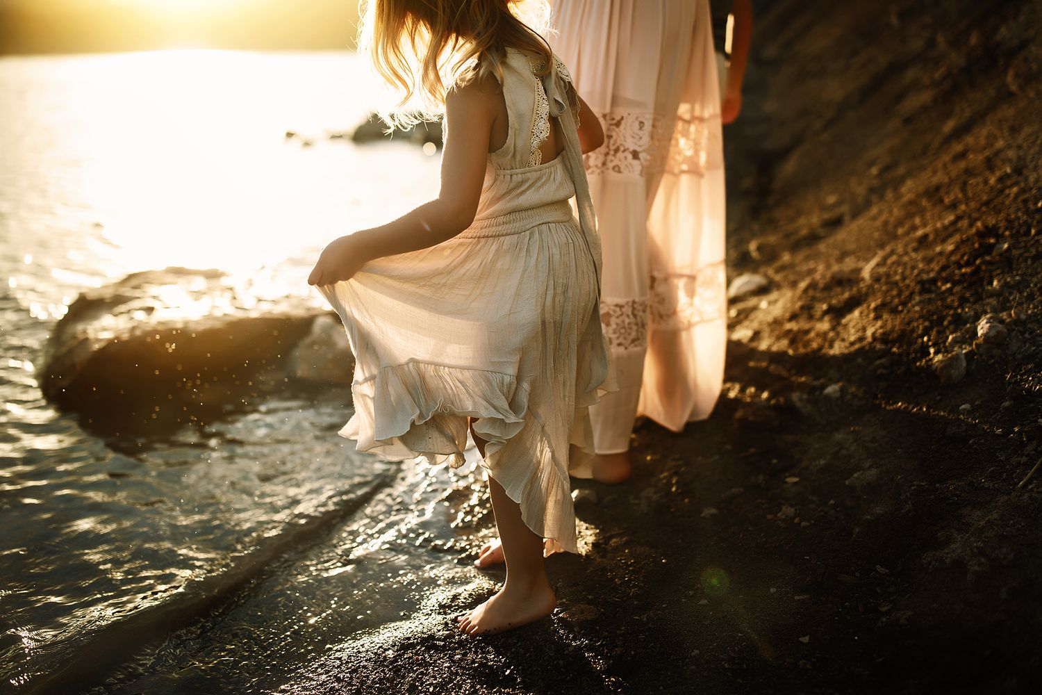 Soft sunlight creates silhouettes on a rocky shoreline during golden hour.