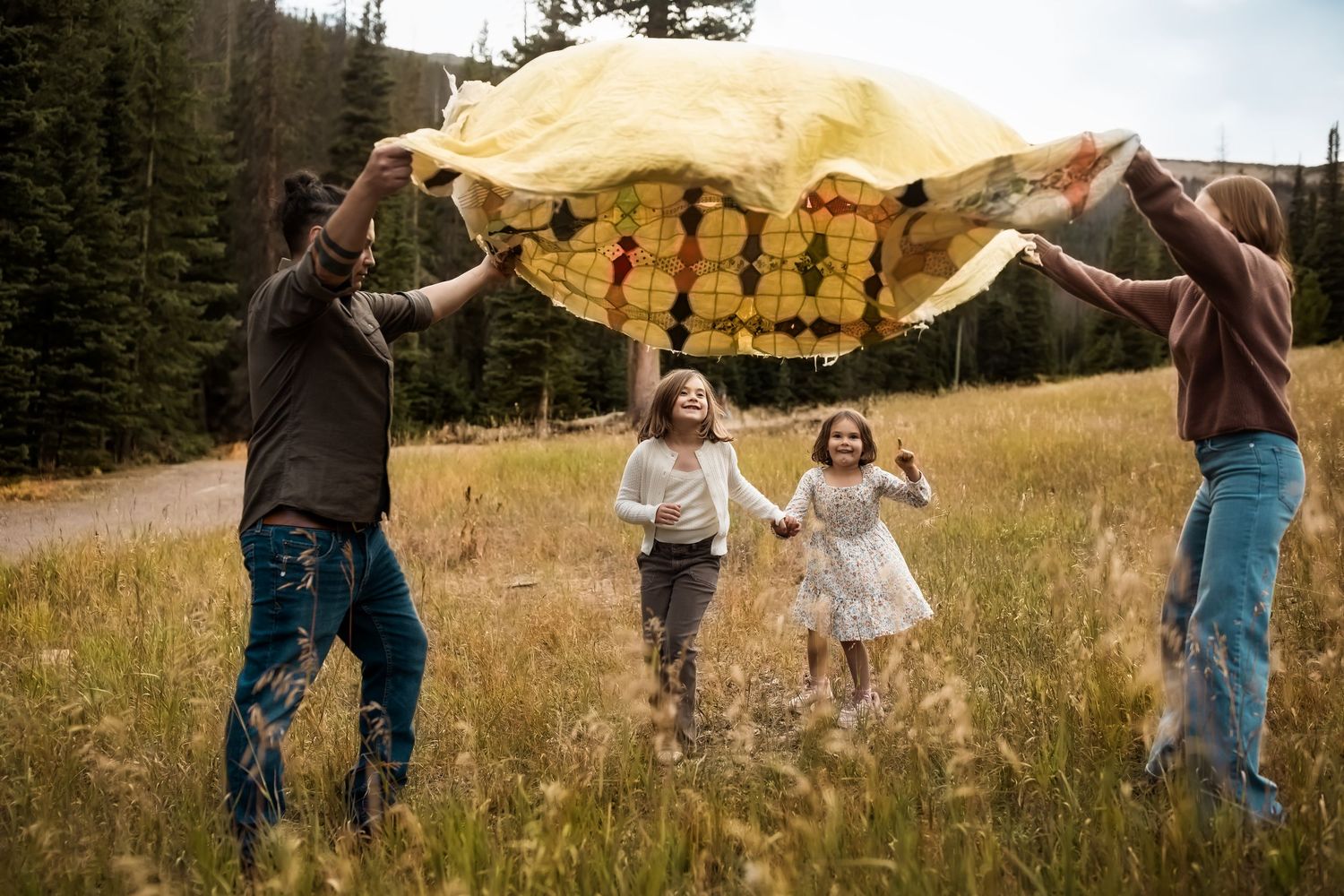 People playing with a yellow blanket in a mountain meadow at sunset.