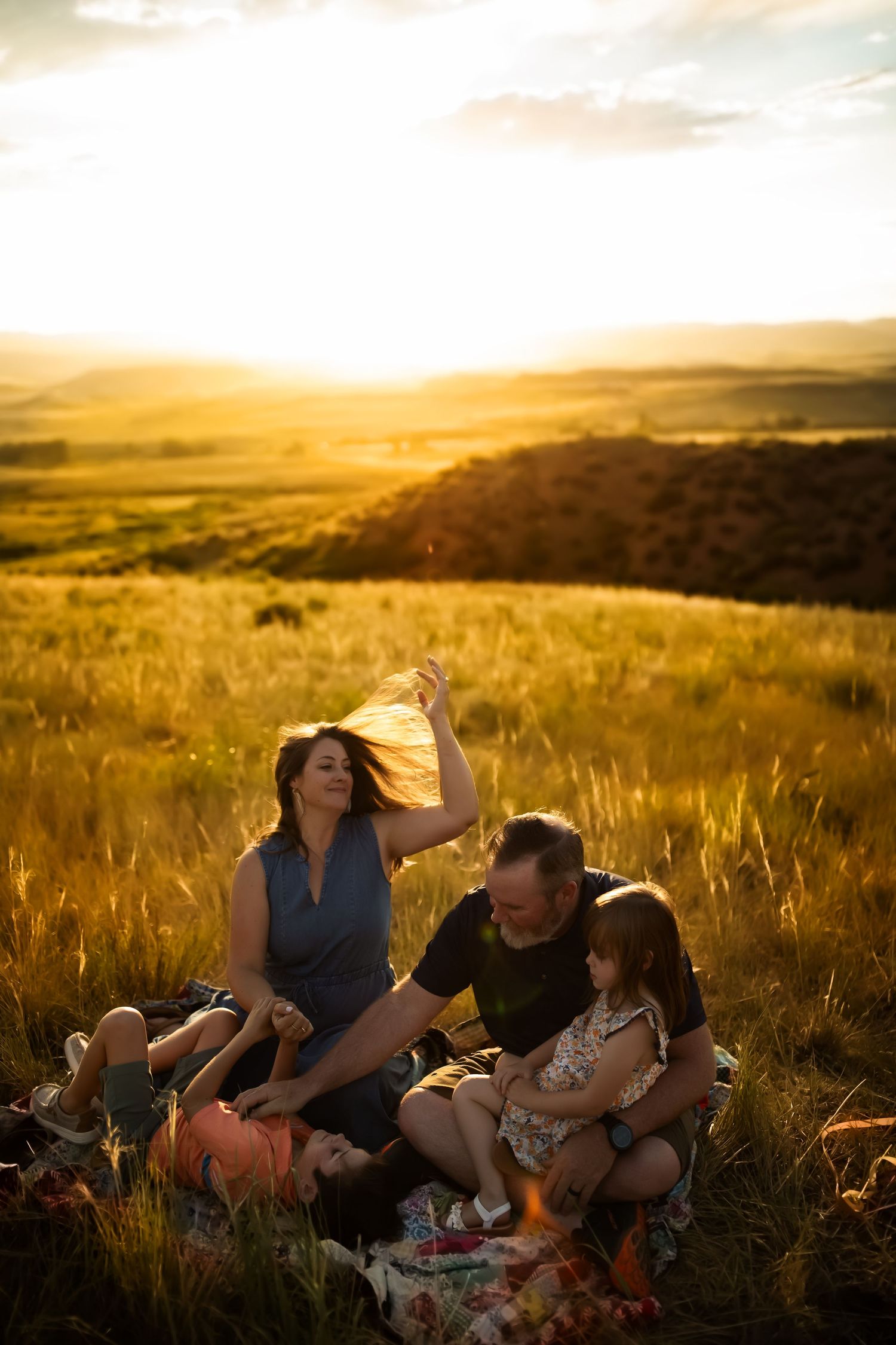 A family relaxes together in a golden field at sunset during a warm summer evening.