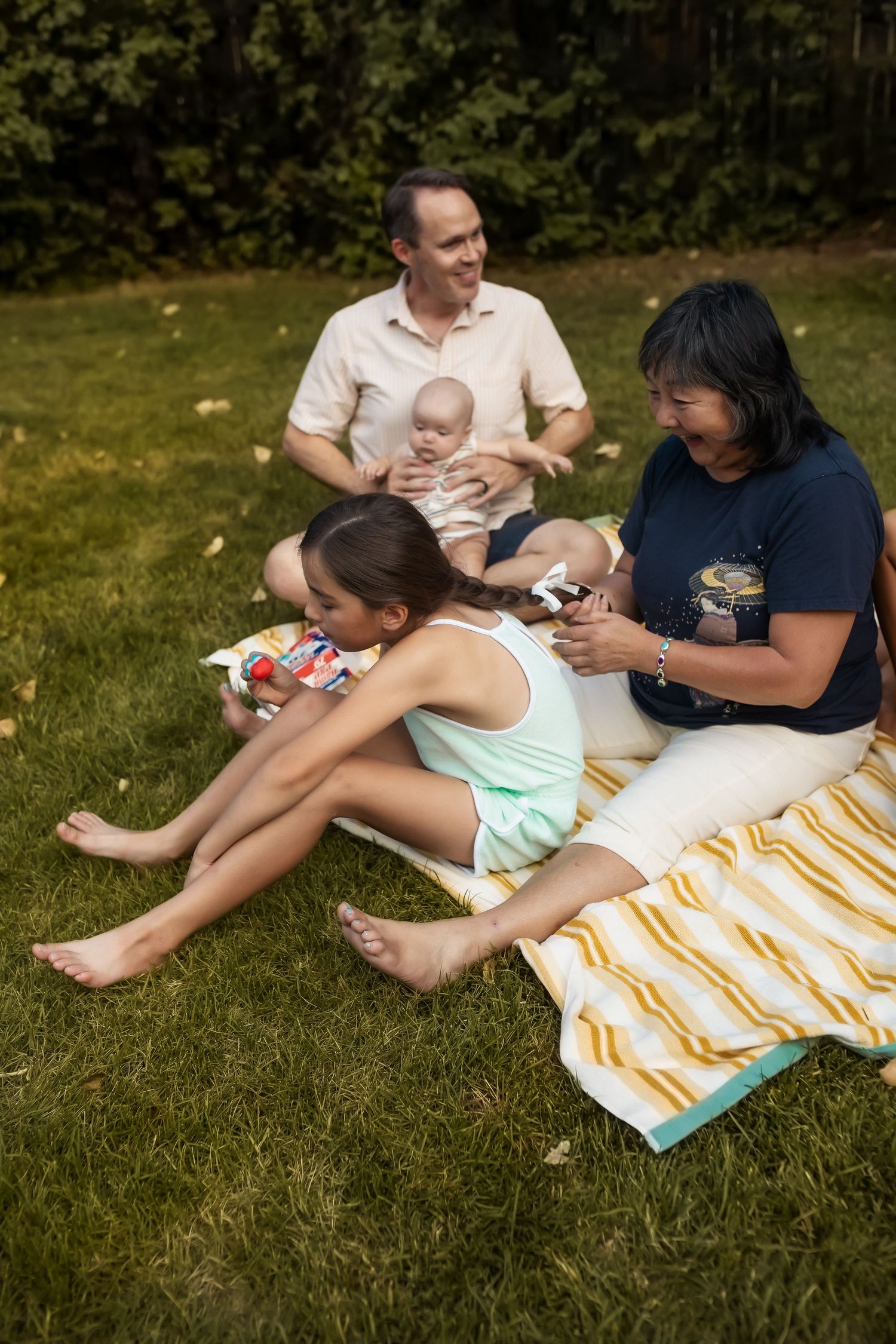 Two people relax on a striped blanket in the grass while enjoying a sunny summer afternoon together.