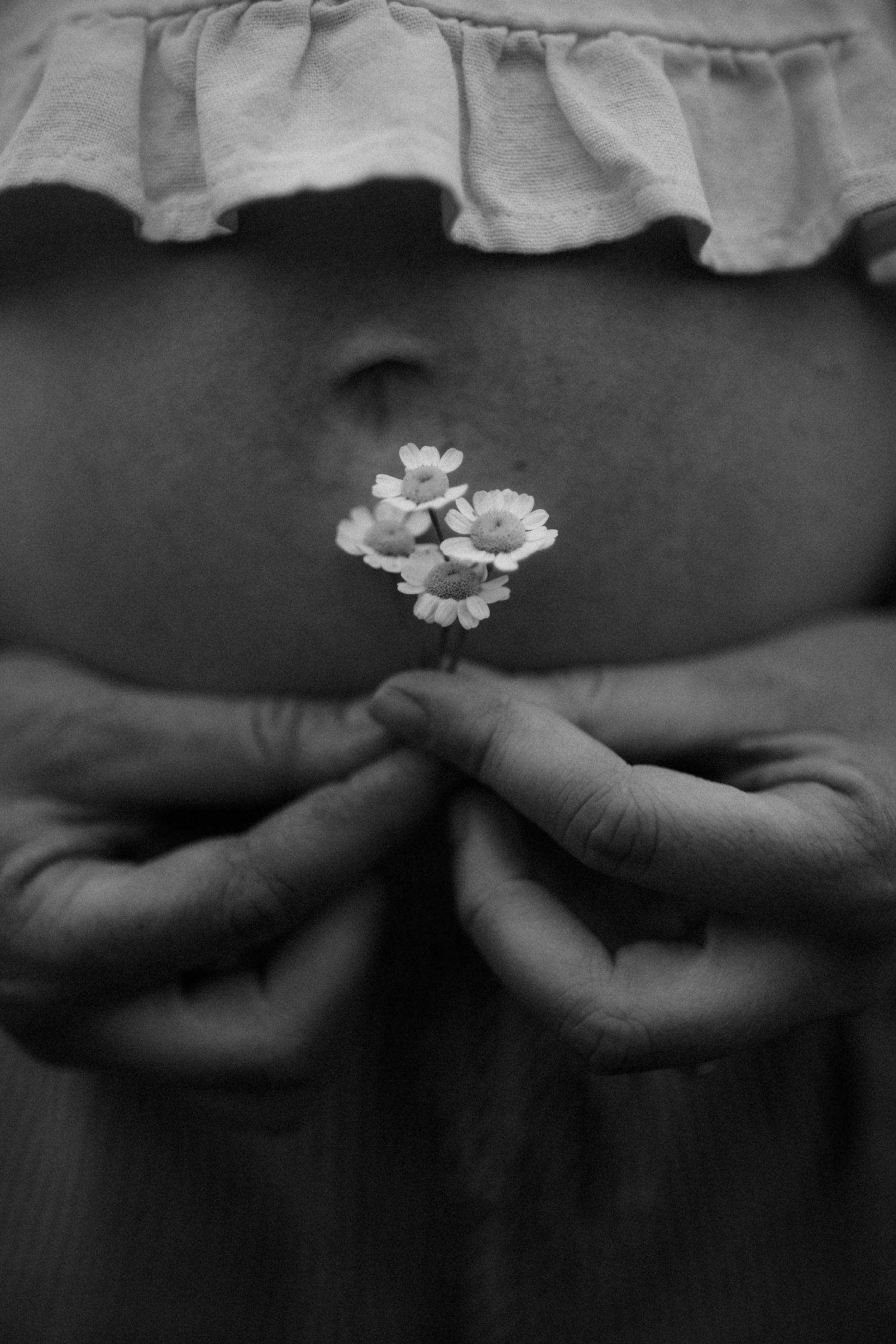 Black and white image of delicate white flowers held against a ruffled fabric background.