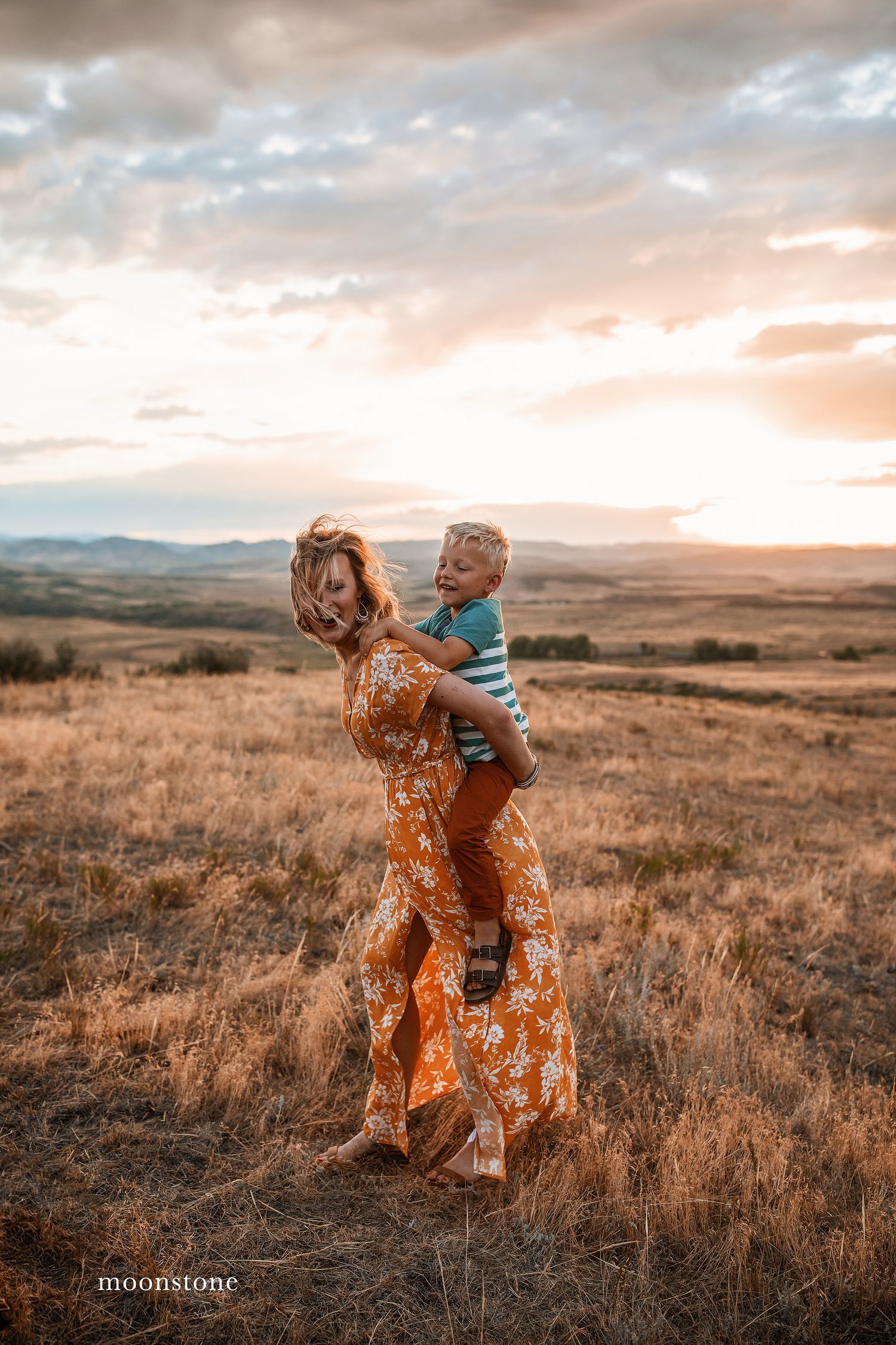 Joyful moment captured in a grassy field with mountains and sunset clouds in the distance.