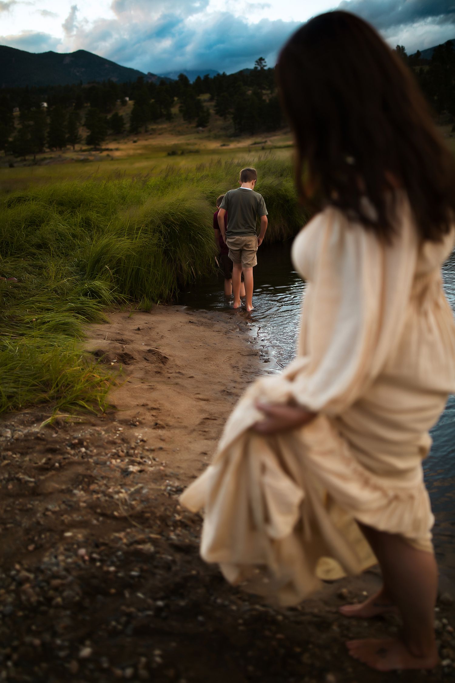 Flowing cream-colored dress captured in motion near mountain stream at sunset.
