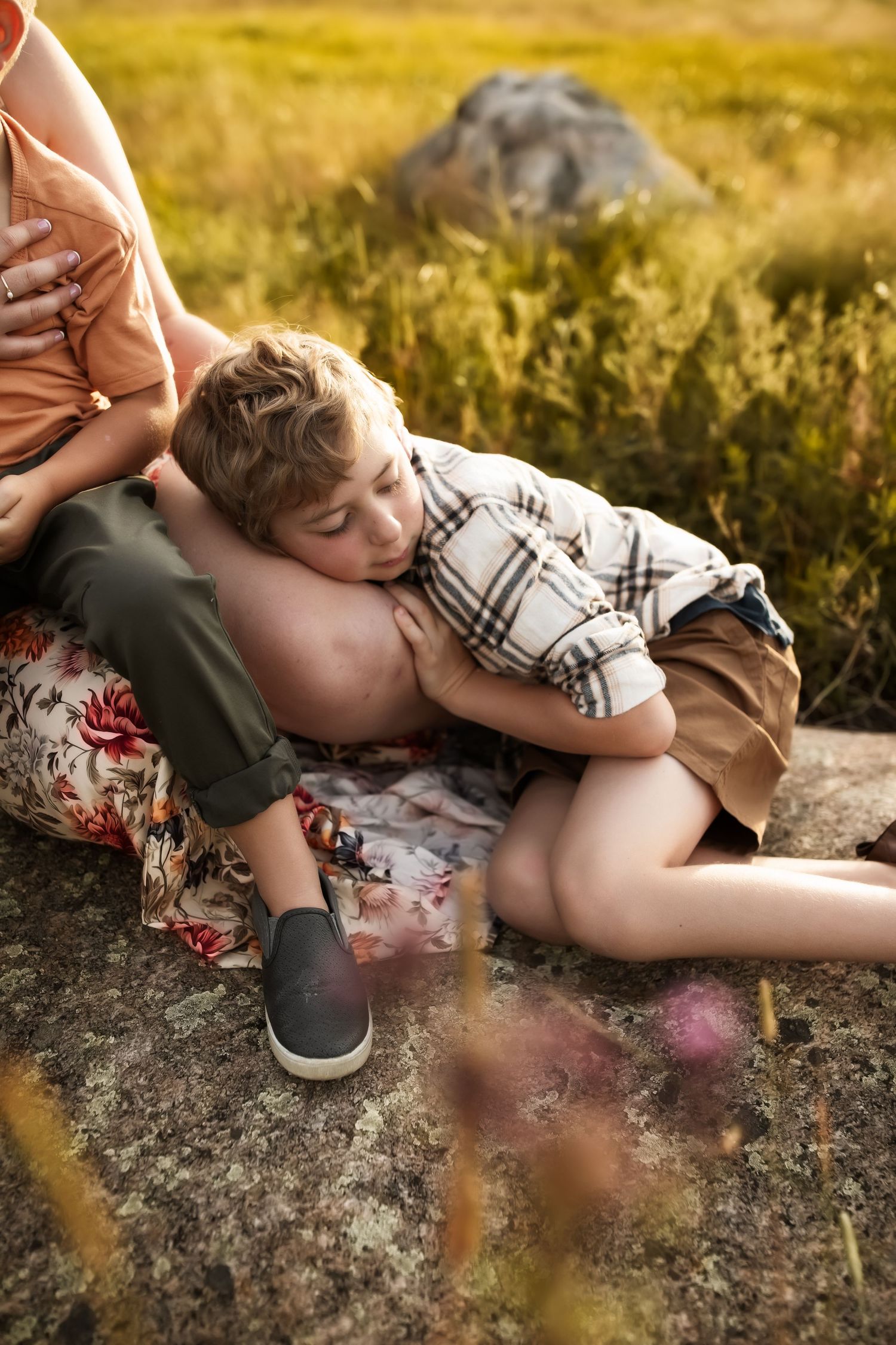 A relaxing summer scene with someone laying on a large rock in a golden field at sunset.