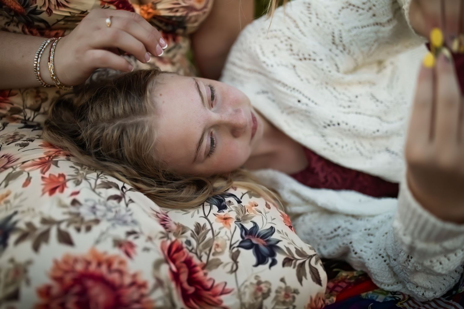Person lying on floral blanket wearing white lace top in outdoor setting.