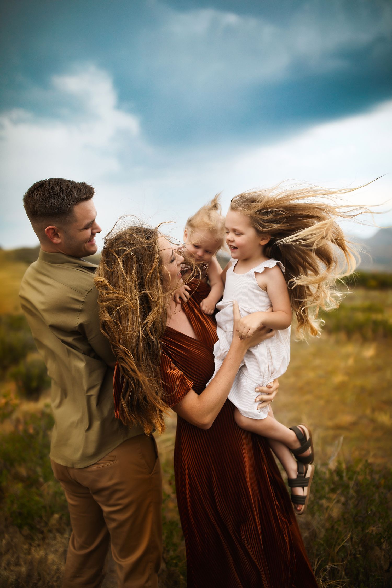 Couple dances and spins together in a field with dramatic cloudy sky backdrop.