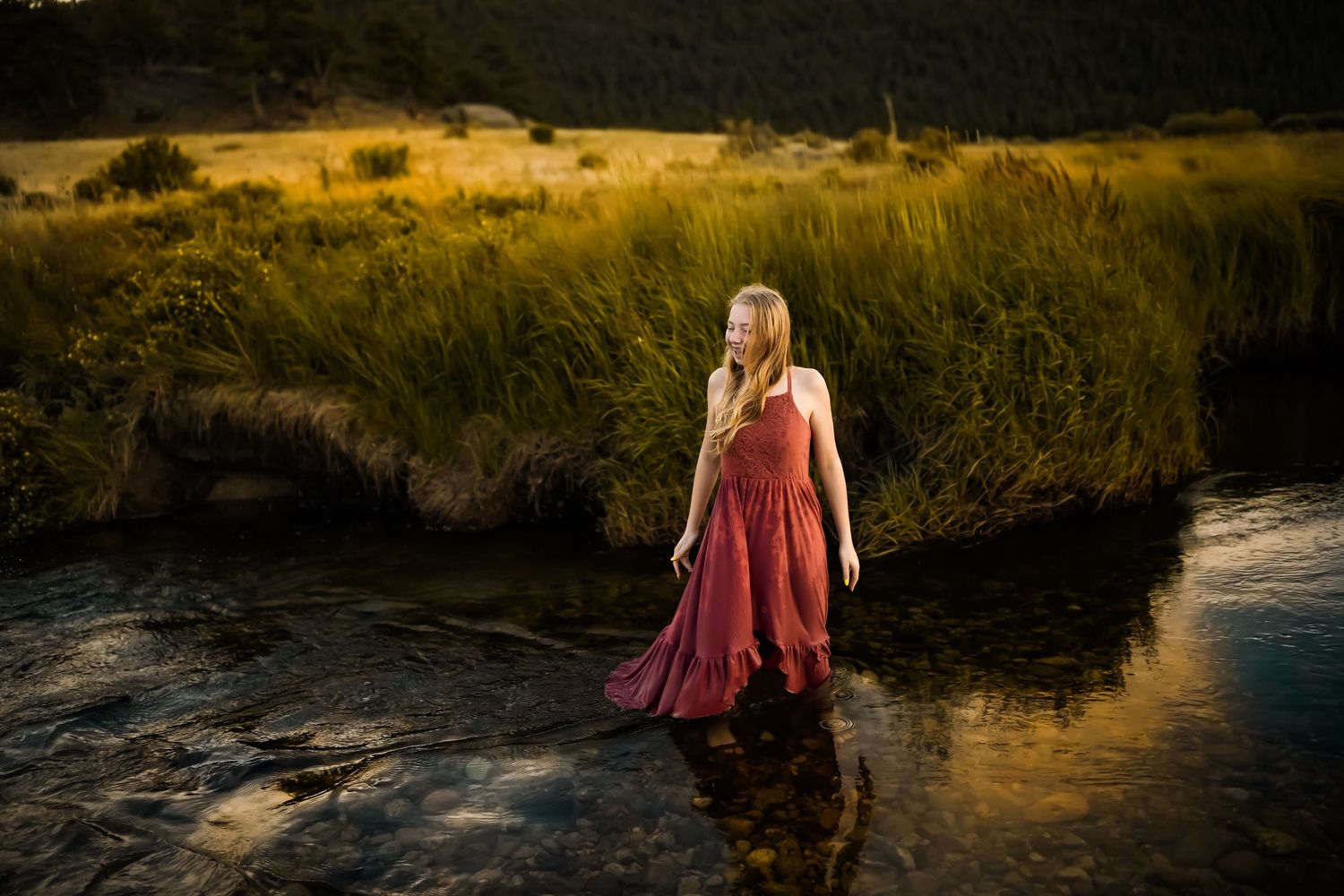 A person in a flowing red dress stands in shallow water at golden hour creating a dreamy outdoor portrait.