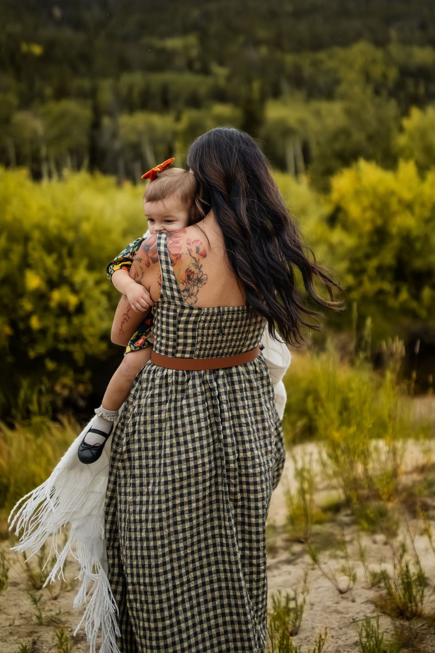 Person in checkered dress holding white fabric against autumn foliage.