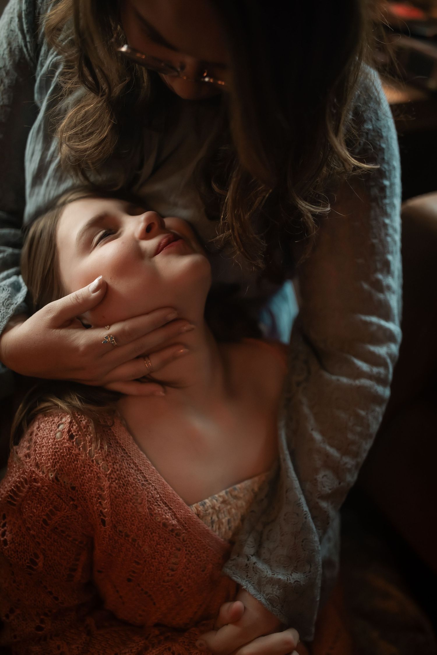A tender moment between a mother and young daughter, with the woman gently cradling the child's face as she looks up lovingly.