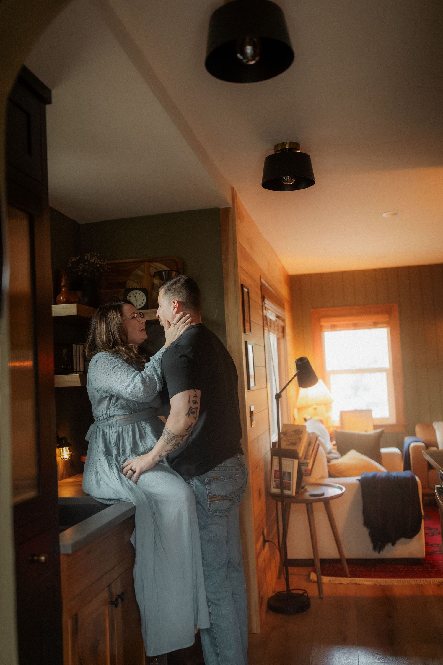 A couple shares a tender moment in a cozy, warmly lit living room, with the woman gently touching the man's face.