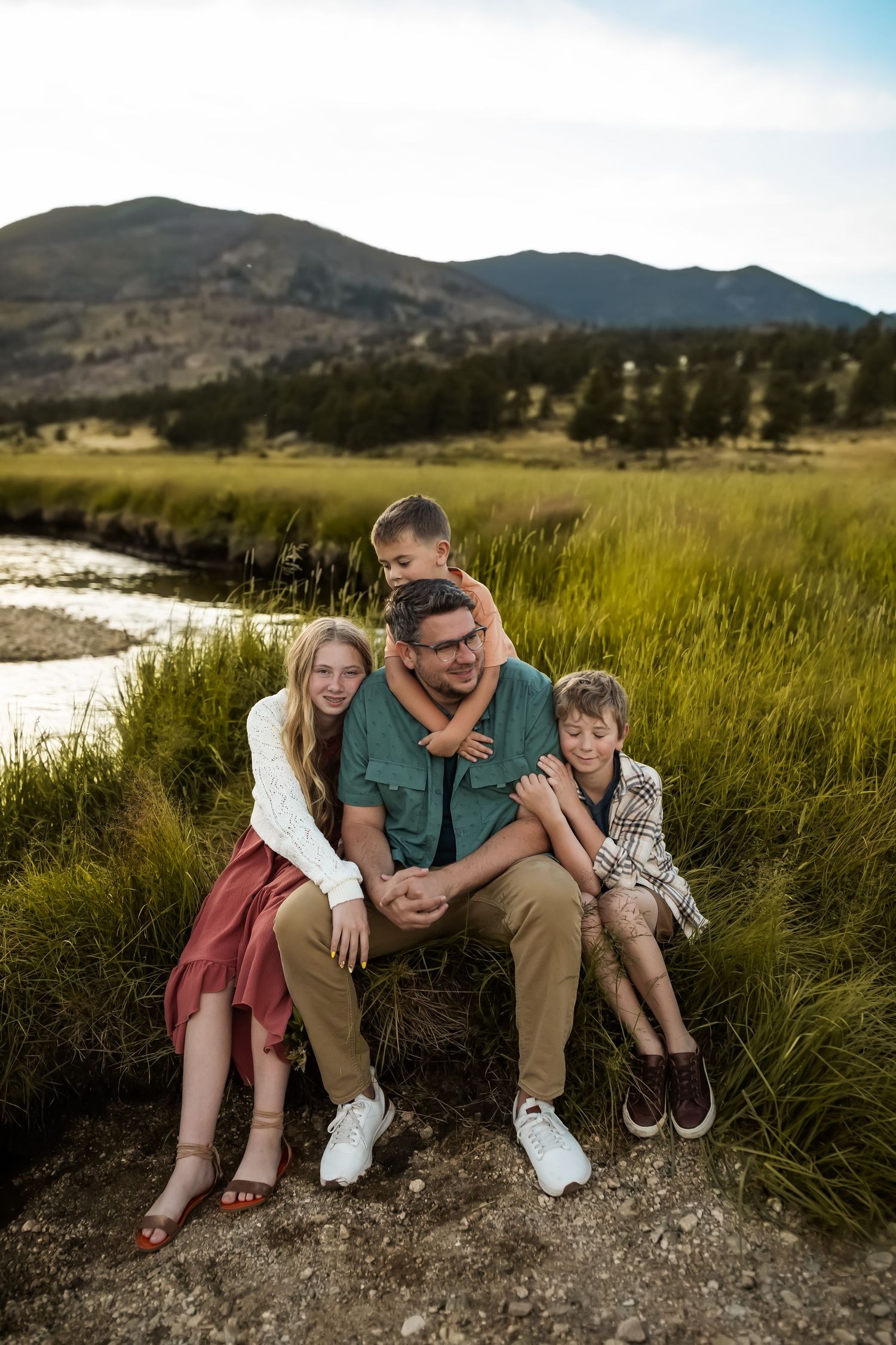Group sitting together on rocky outcrop overlooking mountain meadow at sunset.