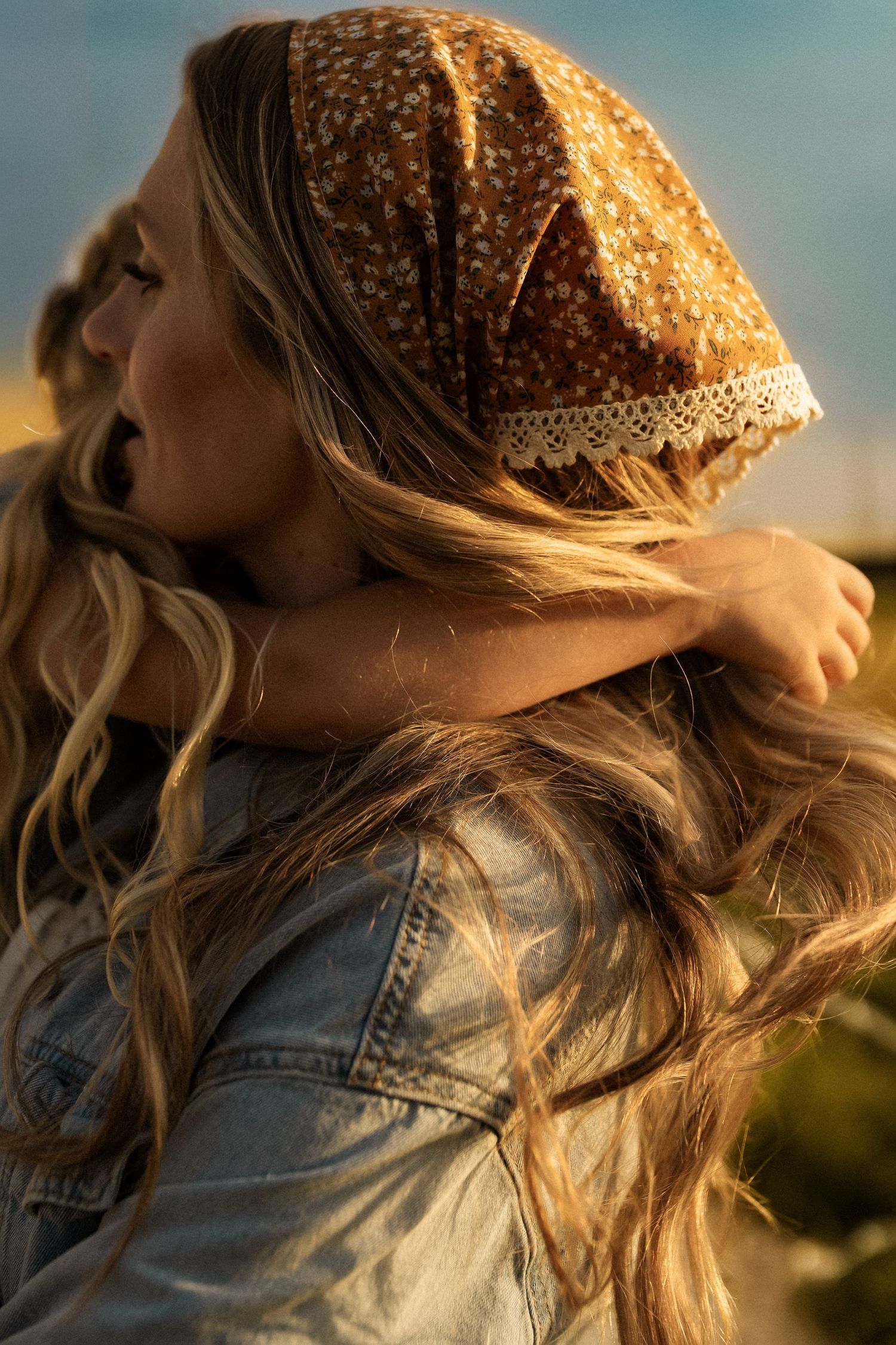 A person wearing a knit beanie and denim jacket gazes upward at sunset with golden light illuminating their profile.