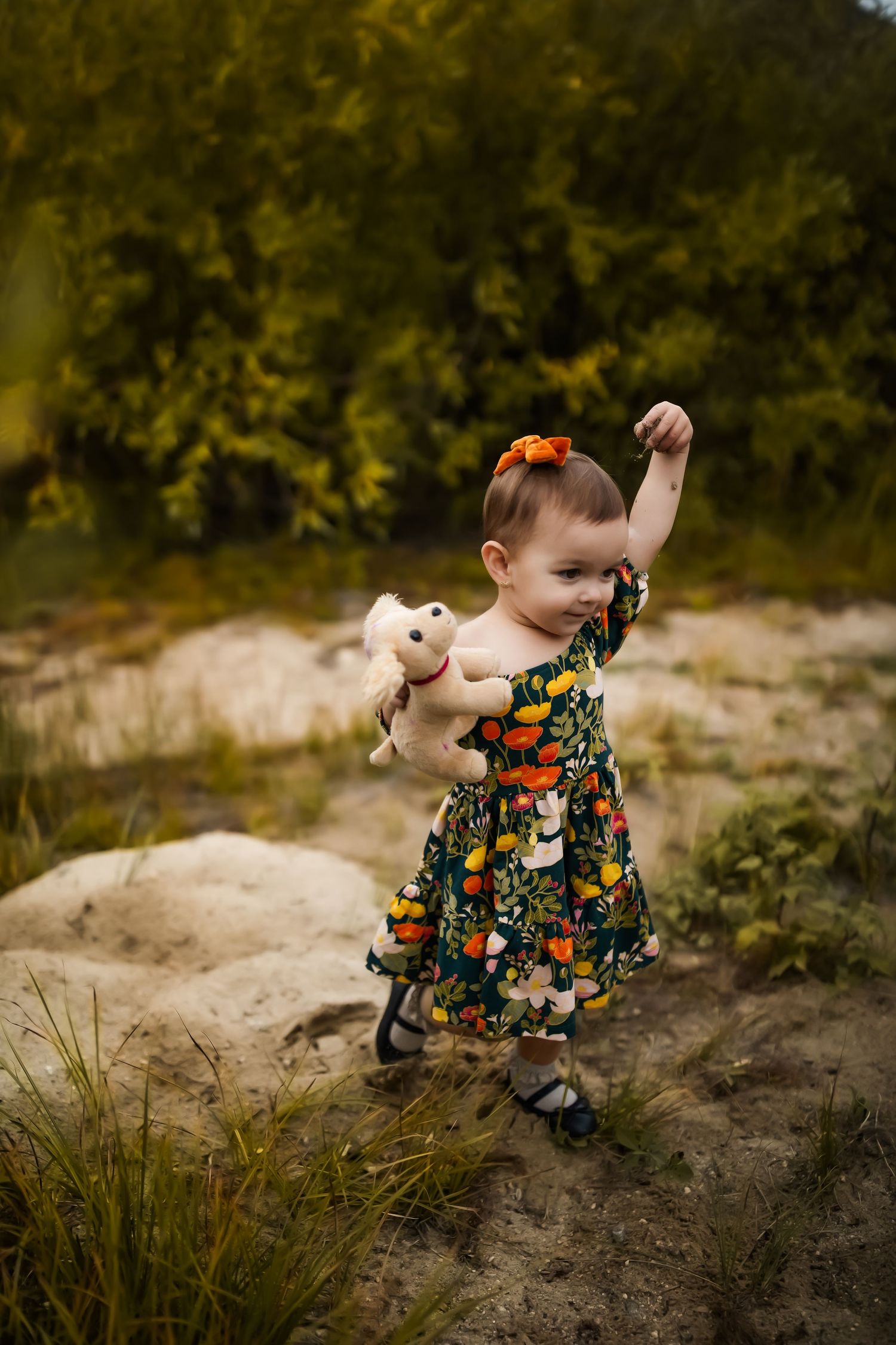 Small child in floral dress playing on natural terrain during golden hour.