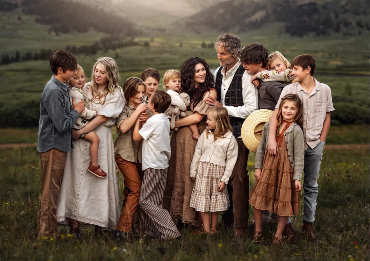 Large family portrait in green meadow, parents with many children in rustic clothing, warm golden light.