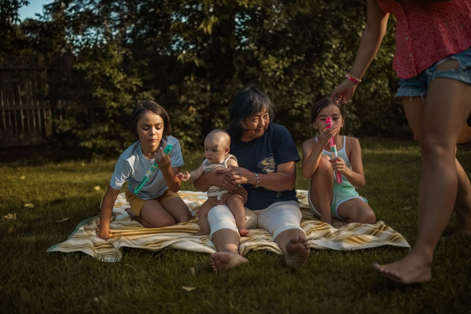 A group sits together reading books on a blanket in a sunny outdoor setting.
