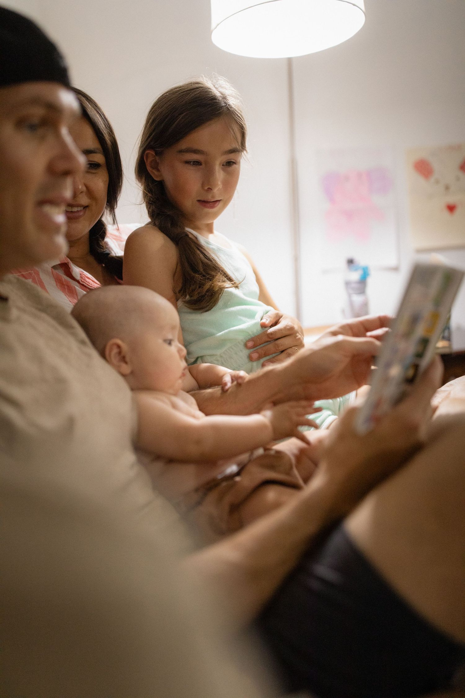 Family sits together on couch reading a book in soft natural lighting.