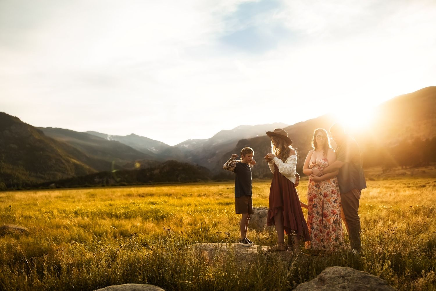 Silhouettes of people in a vast mountain meadow during a dramatic golden sunset.