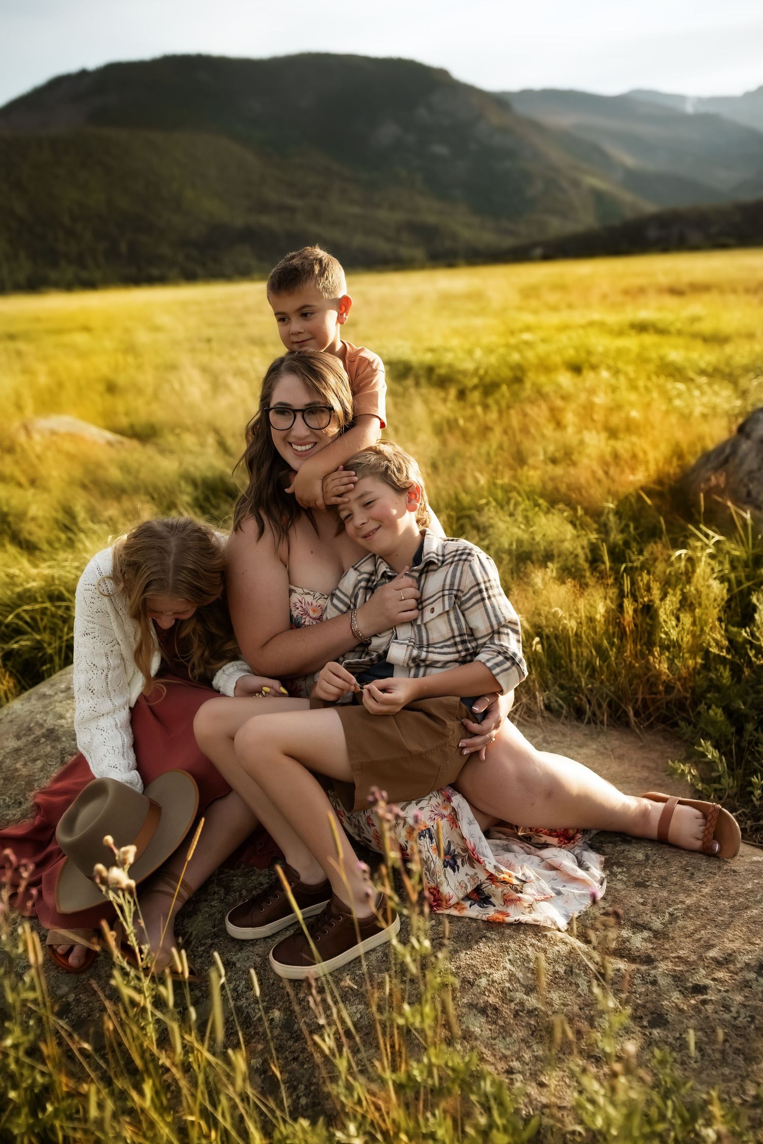 Family cuddling together on rocks in a mountain meadow at golden hour.