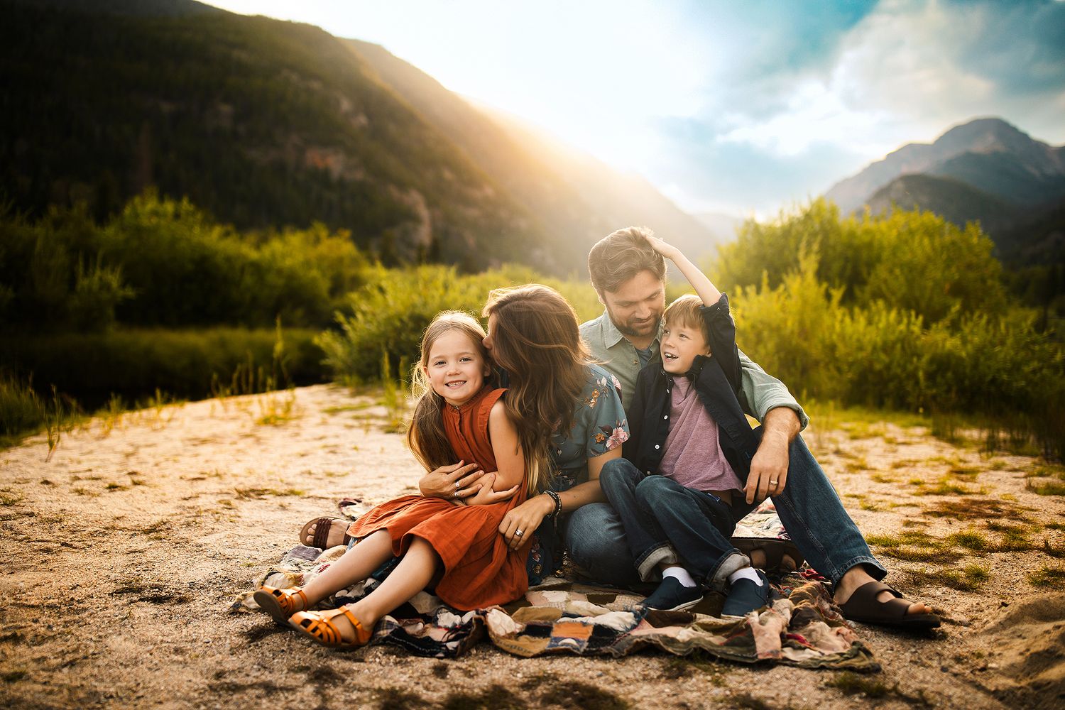 Family lounging together in a scenic mountain meadow at sunset with golden light filtering through.