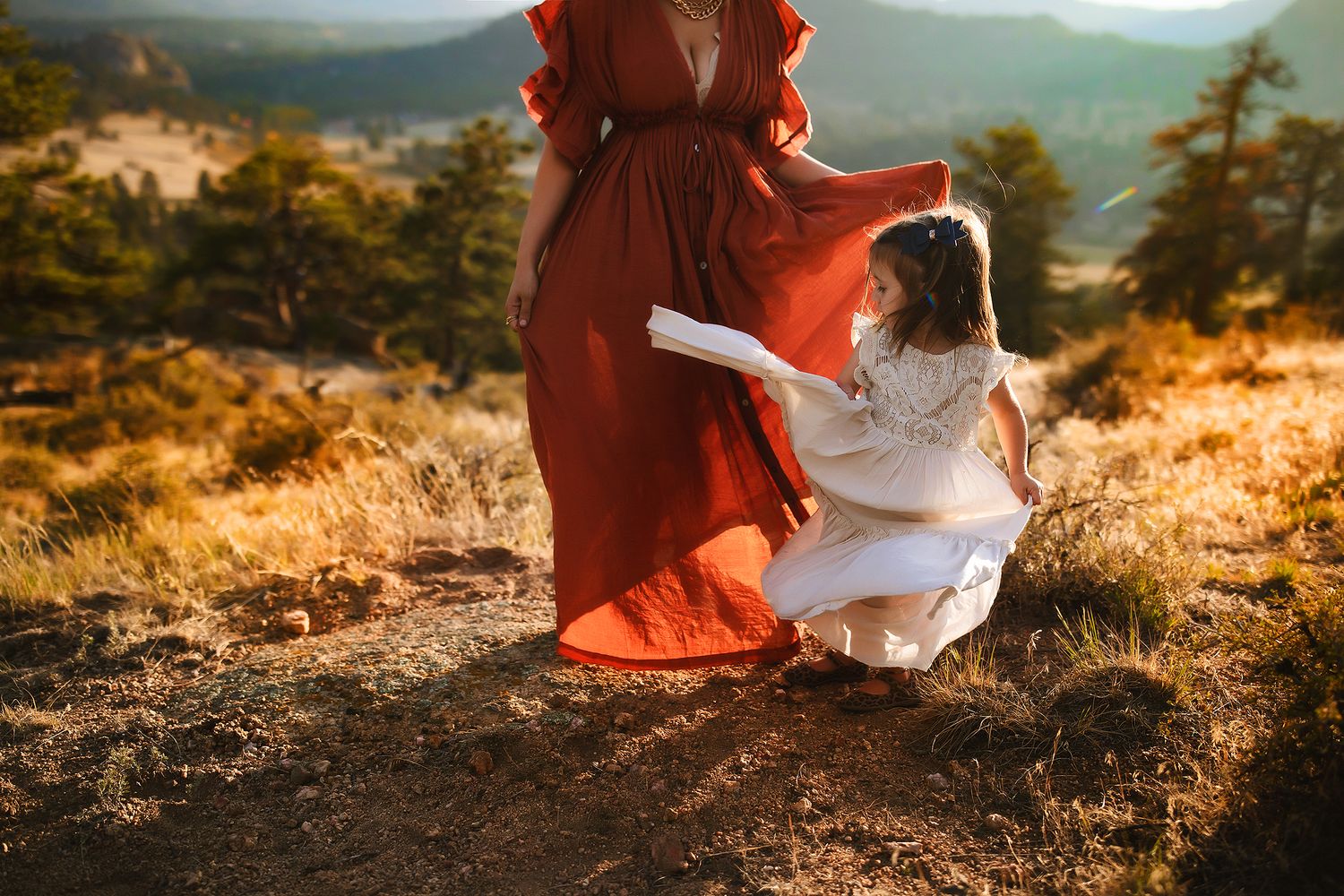 Woman in flowing red dress sitting on mountain overlook at sunset.