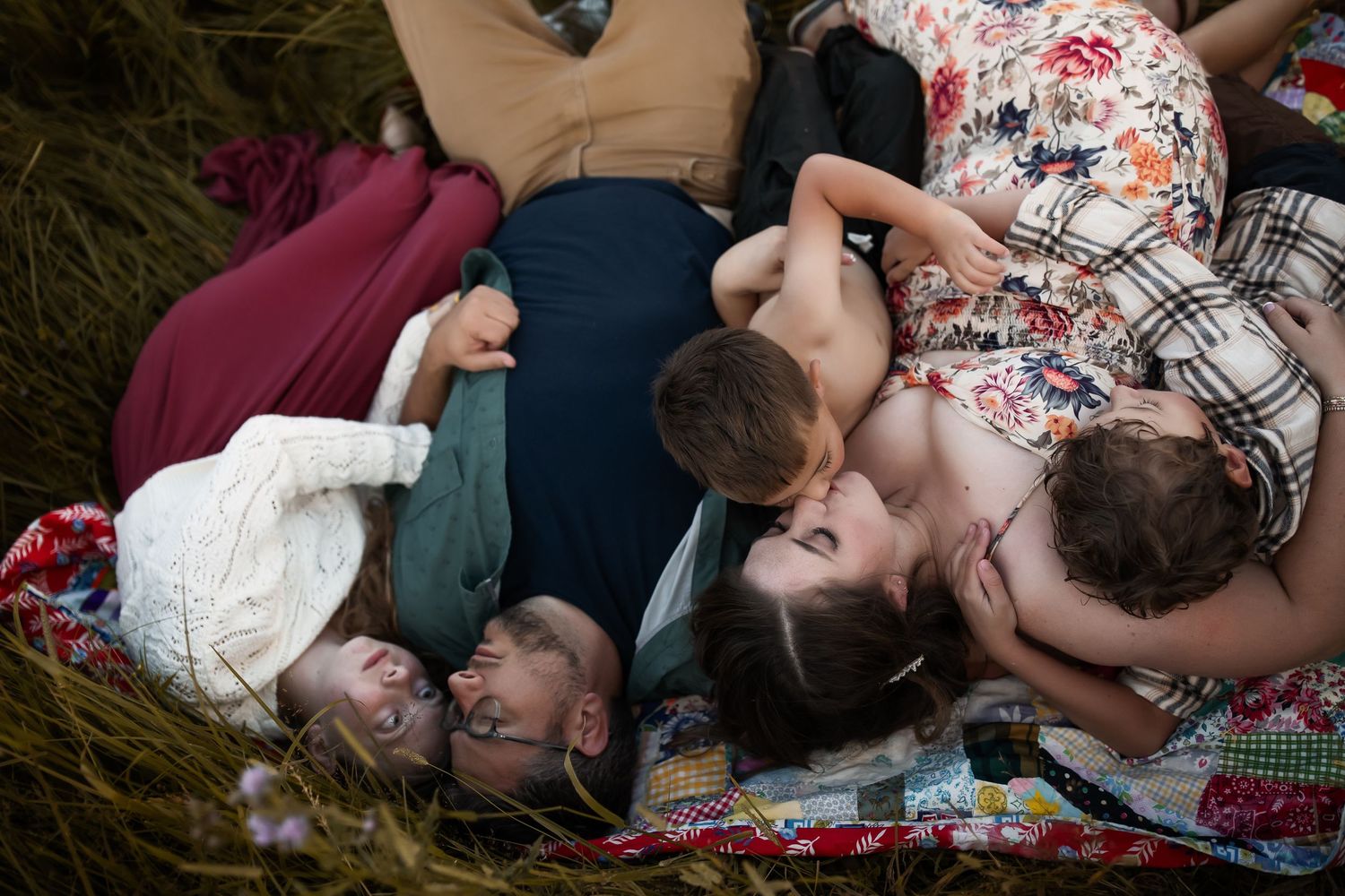 Couple lying together on patterned blanket in outdoor meadow setting.