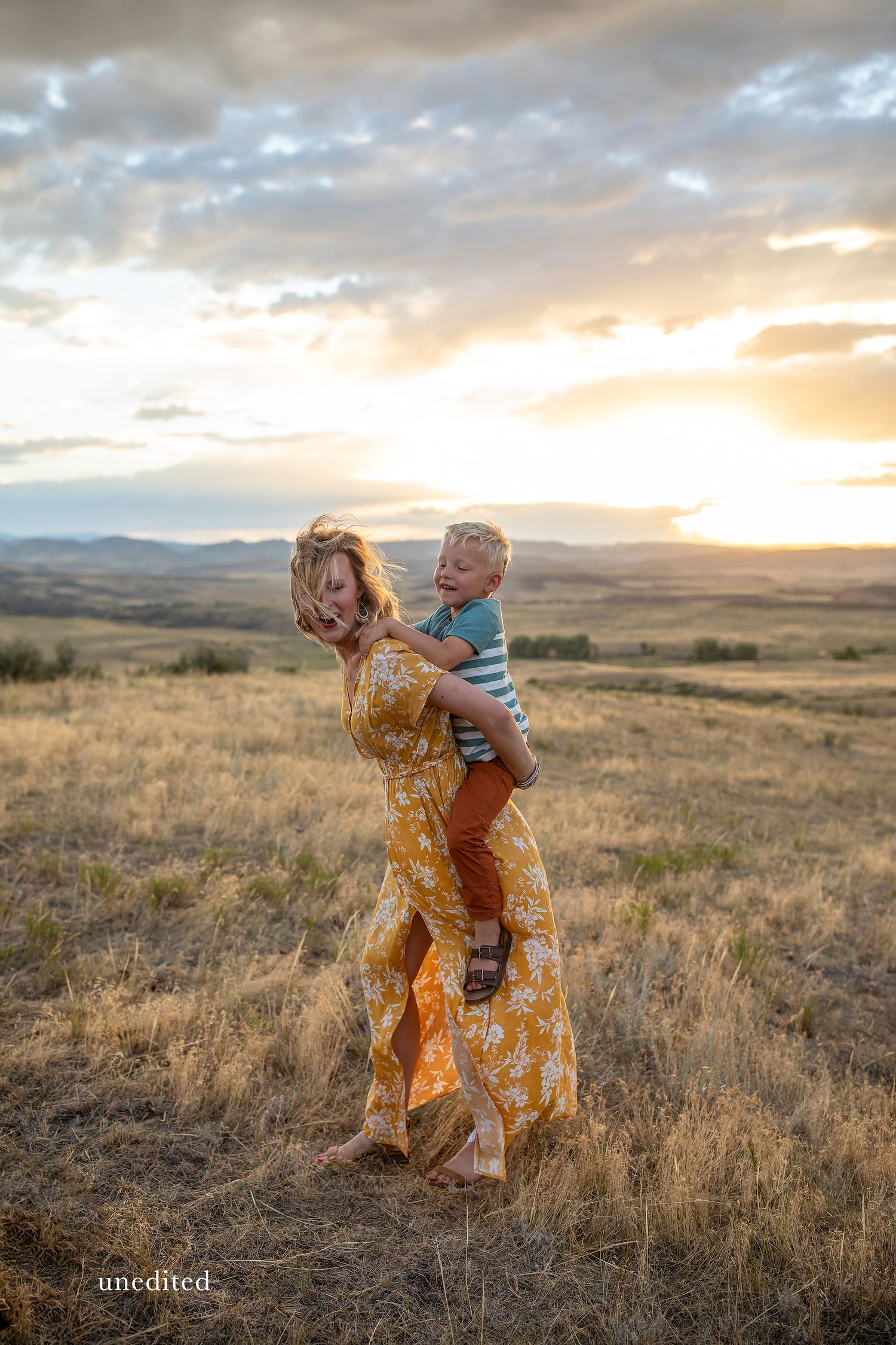Parent and child play together in a golden field at sunset with mountains in the background.