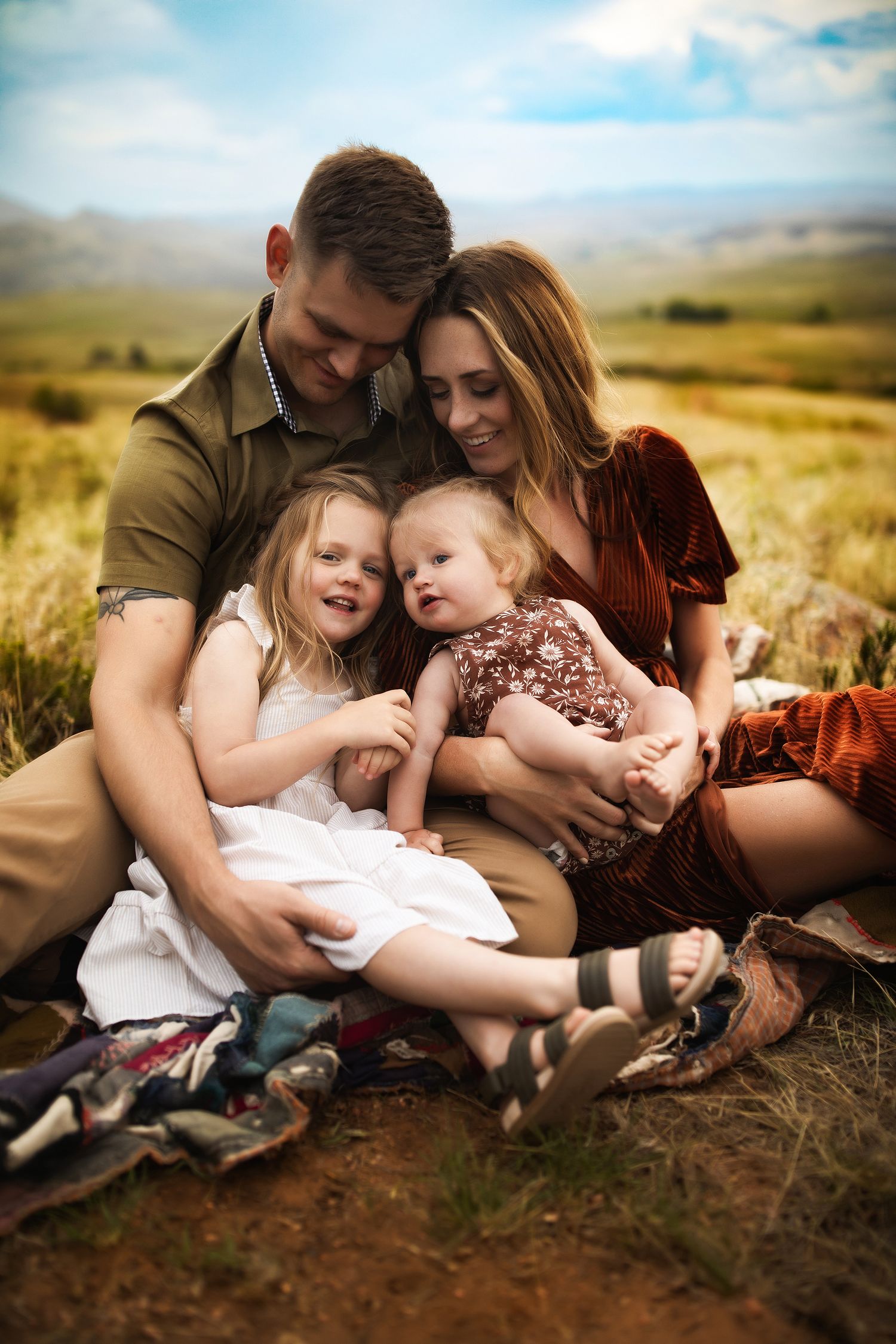 A family sits together in a grassy field sharing an intimate moment at sunset.