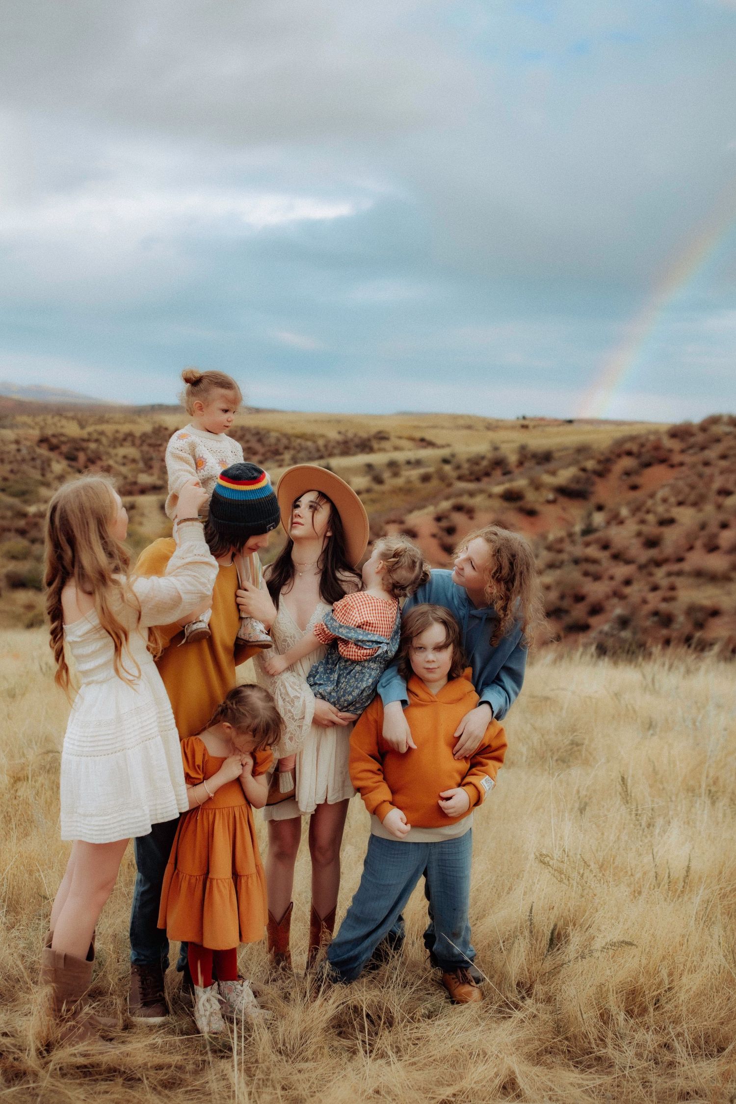Group gathered in desert landscape with rainbow in cloudy sky background.