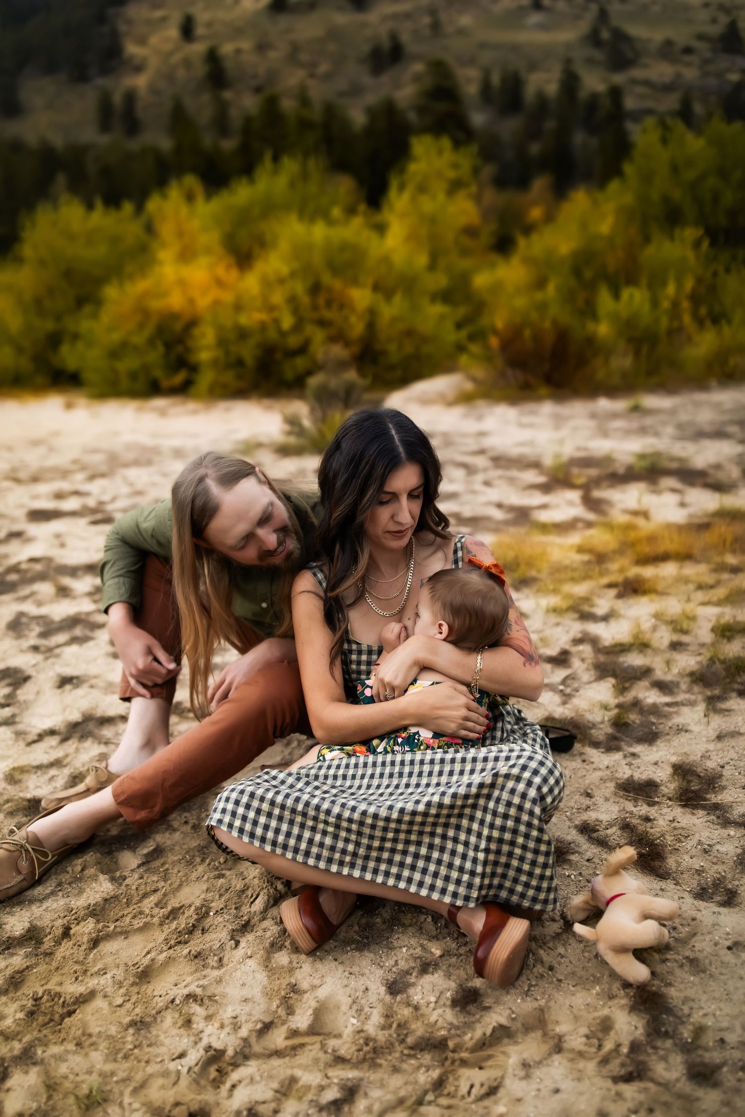 A couple relaxes together on a rocky outcrop surrounded by autumn foliage in the background.